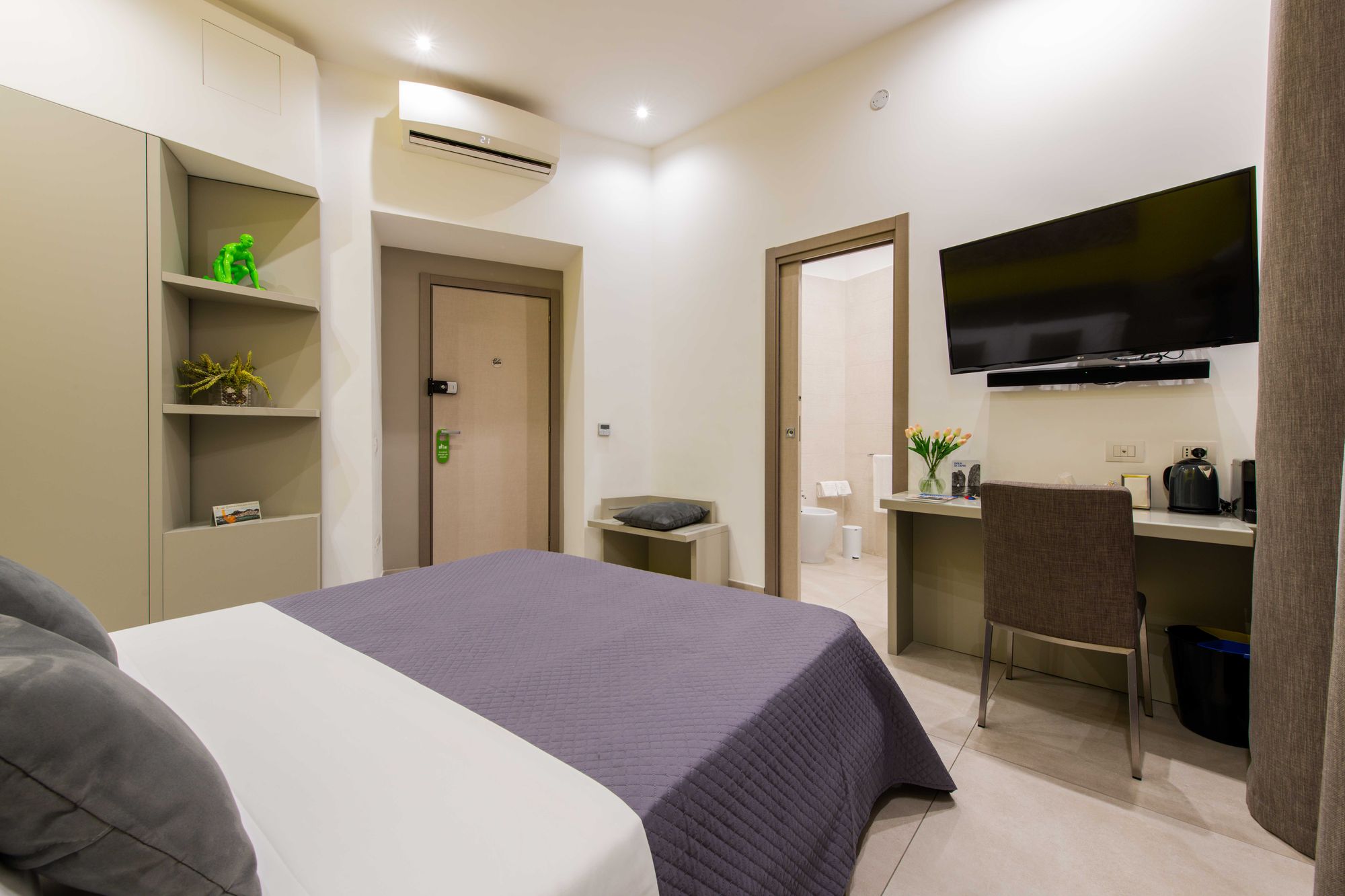 Angolo scrivania con bollitore, macchina da caffè Nespresso e tulipani, TV a parete, porta del bagno aperta e climatizzatore a soffitto - Toledo16 Luxury Suites Napoli
