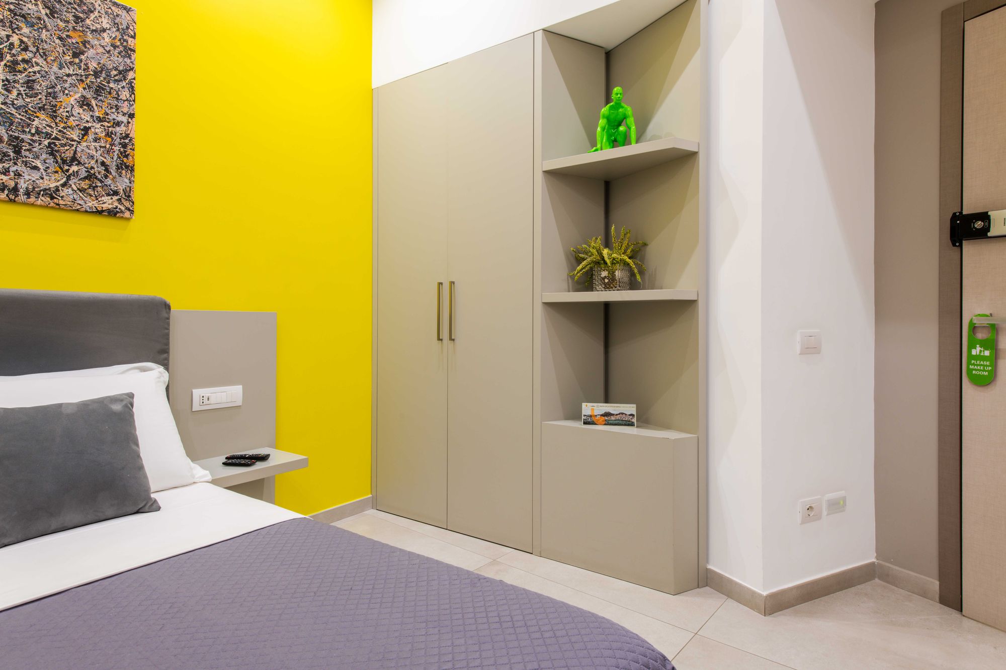 Mensole d'angolo con statuetta verde e piantina decorativa, armadio grigio con maniglie dorate, porta d'ingresso con maniglia verde 'Please make up room' - Toledo16 Luxury Suites Napoli