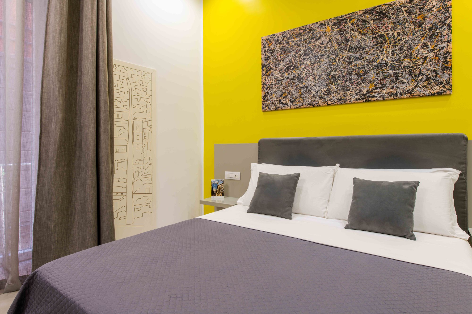 Testiera in velluto grigio con cuscini bianchi e cuscini decorativi grigi, quadro astratto su parete gialla e pannello decorativo con skyline di Napoli - Toledo16 Luxury Suites Napoli