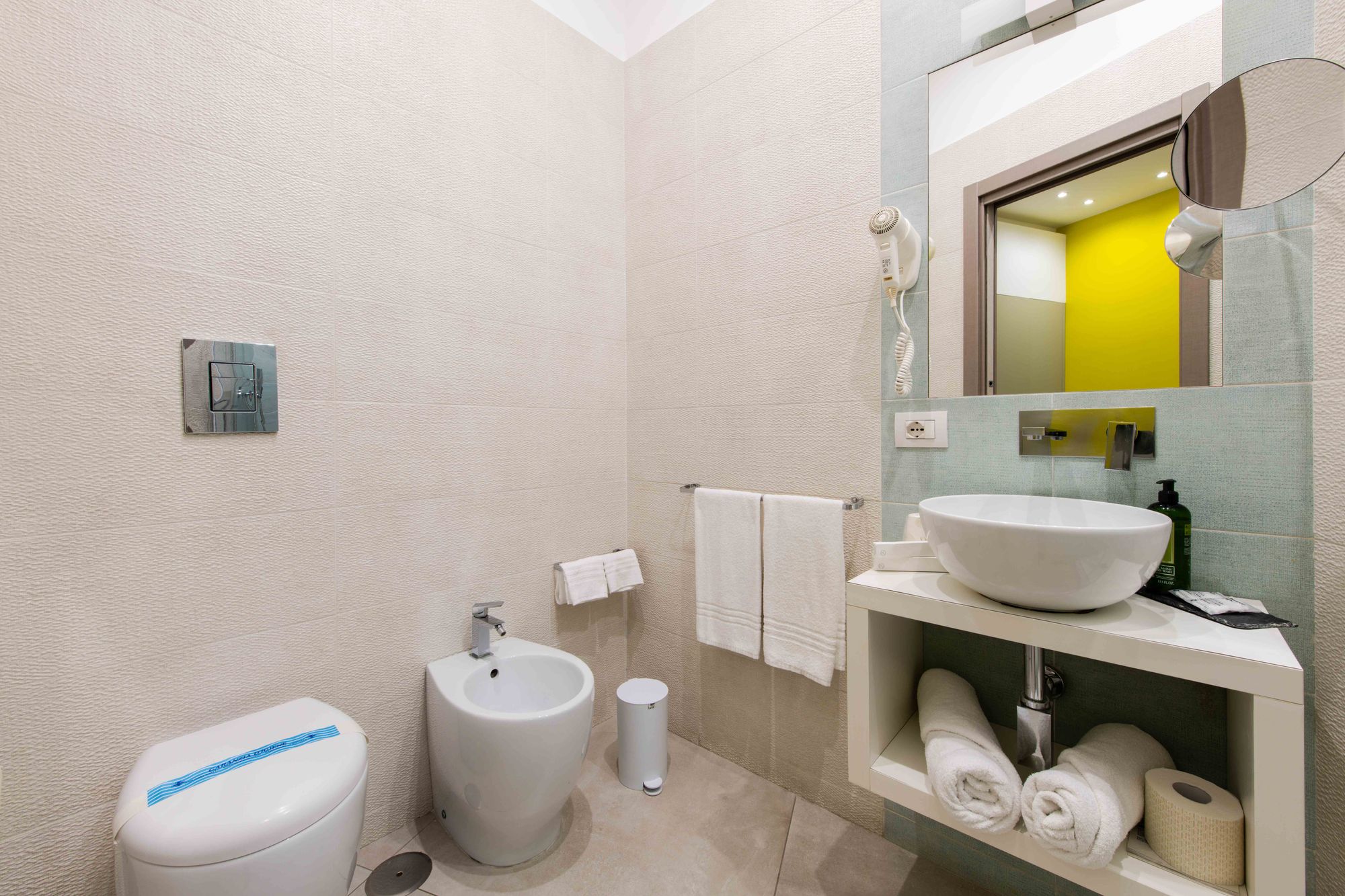 Bagno con WC e bidet in ceramica bianca, asciugamani su portasalviette, lavabo a bacinella su mobile bianco con asciugamani arrotolati - Toledo16 Luxury Suites Napoli