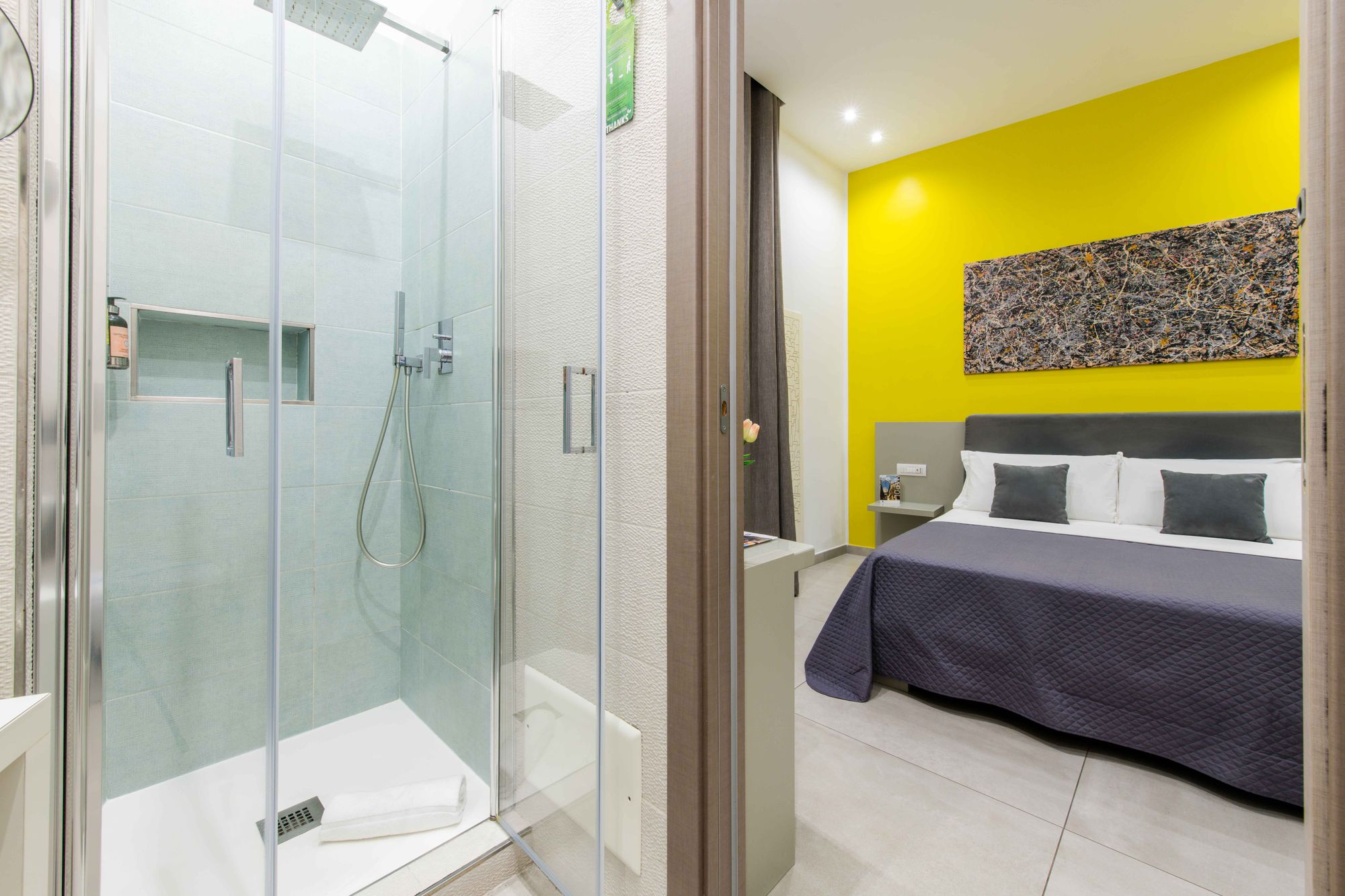Box doccia in vetro con soffione doccia a pioggia, doccetta e nicchia portaoggetti su piastrelle azzurre, vista sulla camera con parete gialla - Toledo16 Luxury Suites Napoli