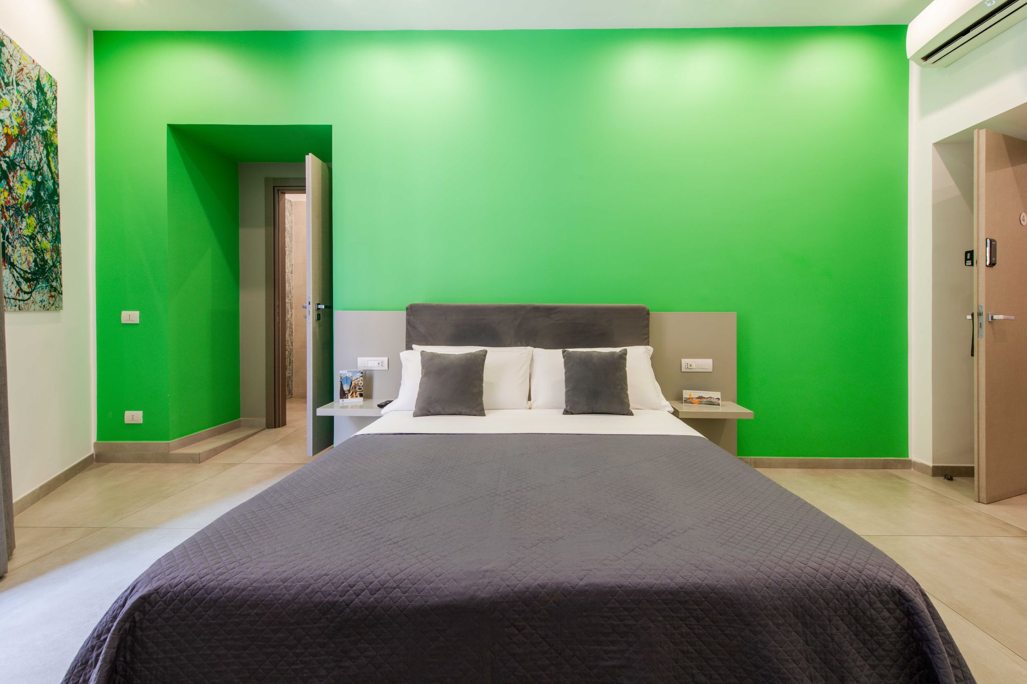 Vista d'insieme della camera doppia Deluxe con letto grigio antracite, parete verde smeraldo, quadro astratto e porta del bagno aperta - Toledo16 Luxury Suites Napoli