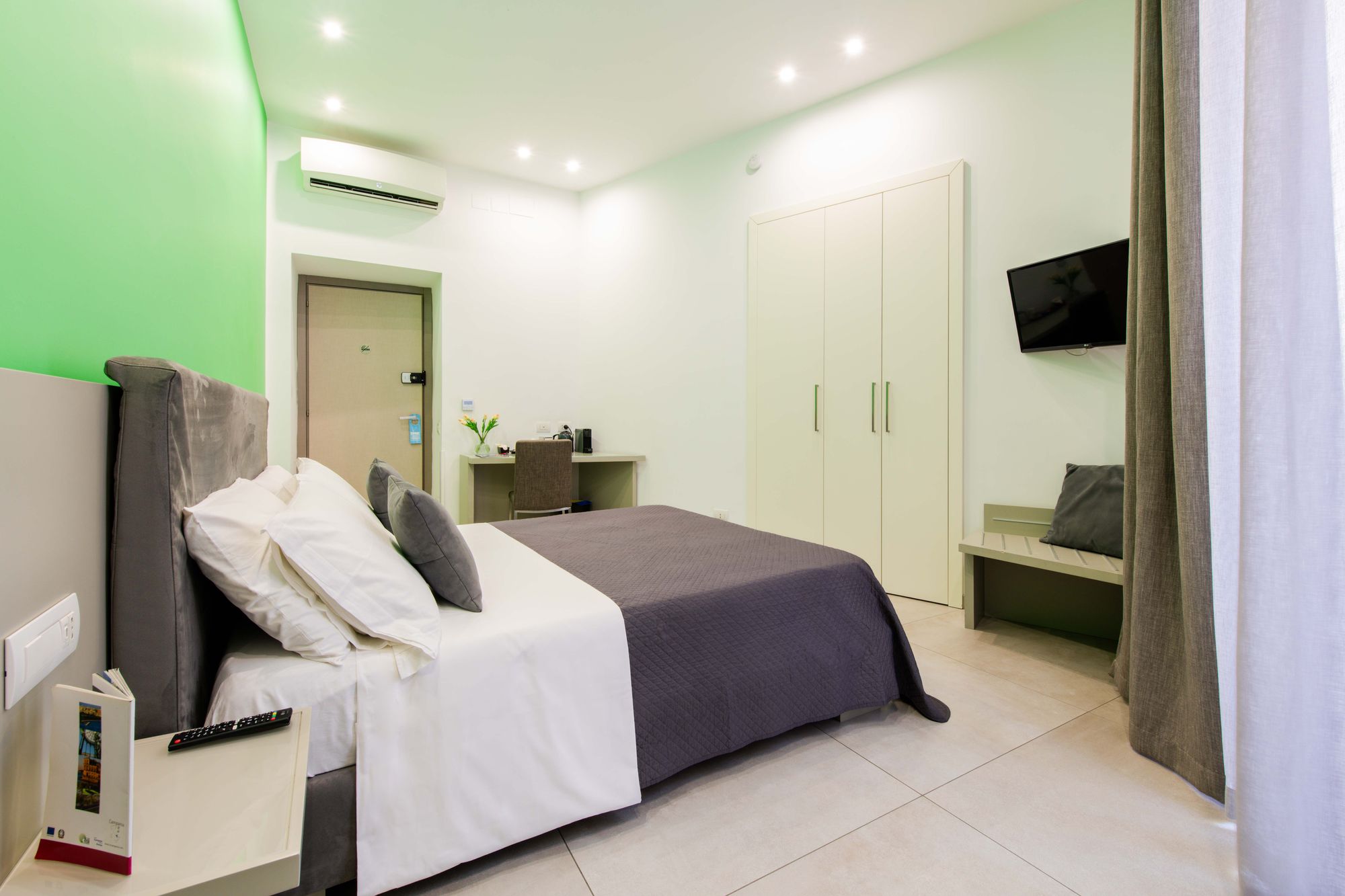 Angolo camera con armadio bianco, TV a parete, climatizzatore e scrivania con tulipani e macchina da caffè - Toledo16 Luxury Suites Napoli