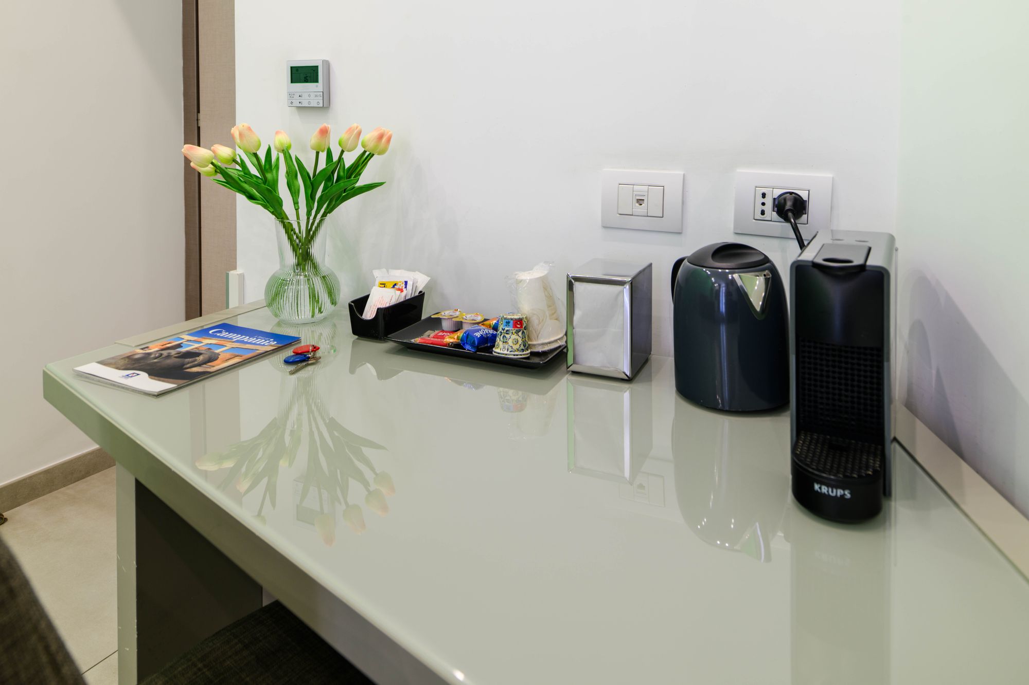 Angolo cortesia con bollitore, macchina Nespresso Krups, vaso di tulipani e set da tè su scrivania in vetro - Toledo16 Luxury Suites Napoli