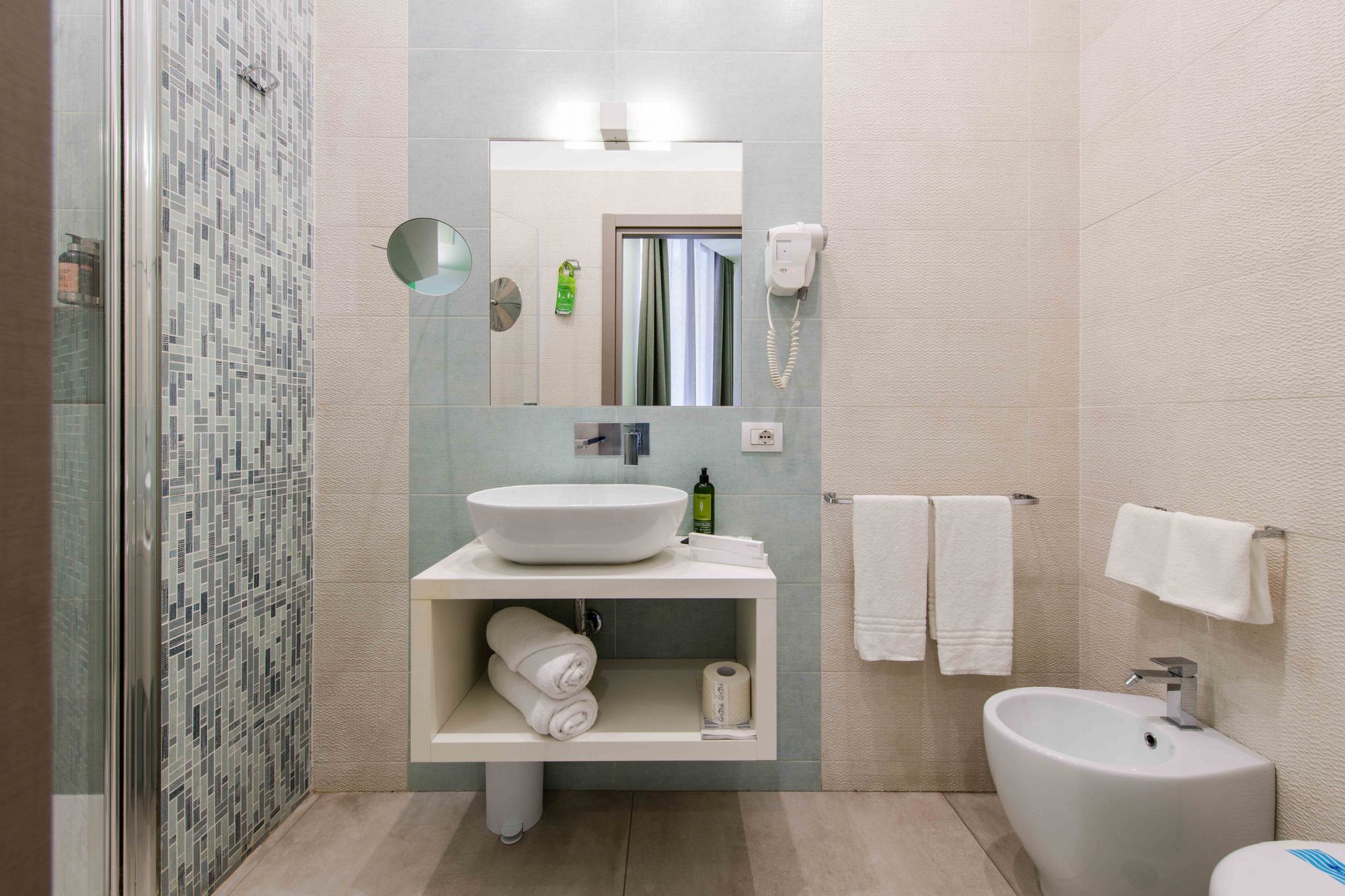 Bagno con lavabo bianco da appoggio, doccia con parete in mosaico verde acqua, asciugacapelli e bidet - Toledo16 Luxury Suites Napoli