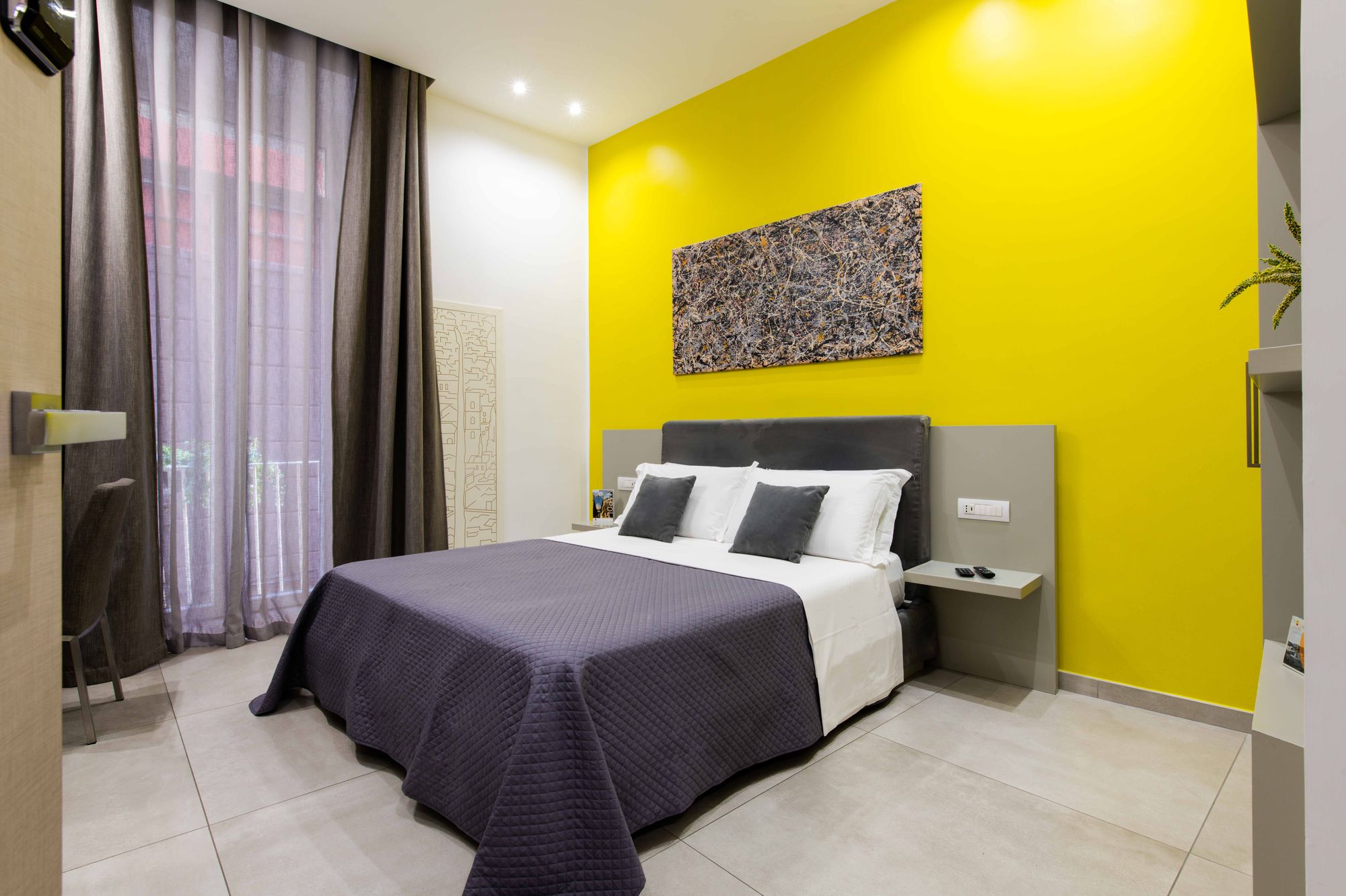 Camera doppia Deluxe con parete gialla e letto con copriletto grigio antracite, a pochi passi dalla metro Dante - Toledo16 Luxury Suites Napoli