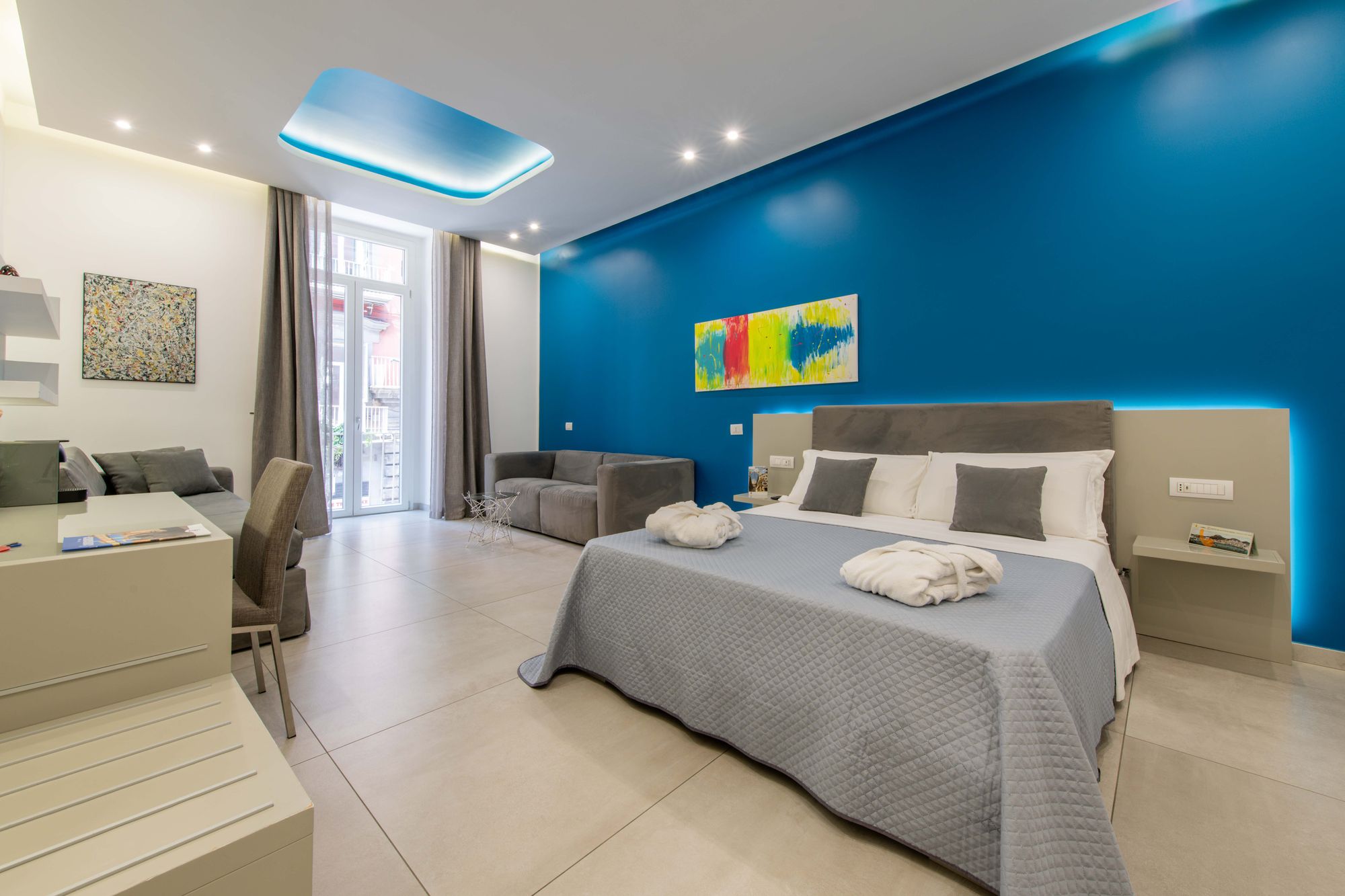 Suite con parete blu, accappatoi sul letto e quadro colorato - Toledo16 Luxury Suites Napoli