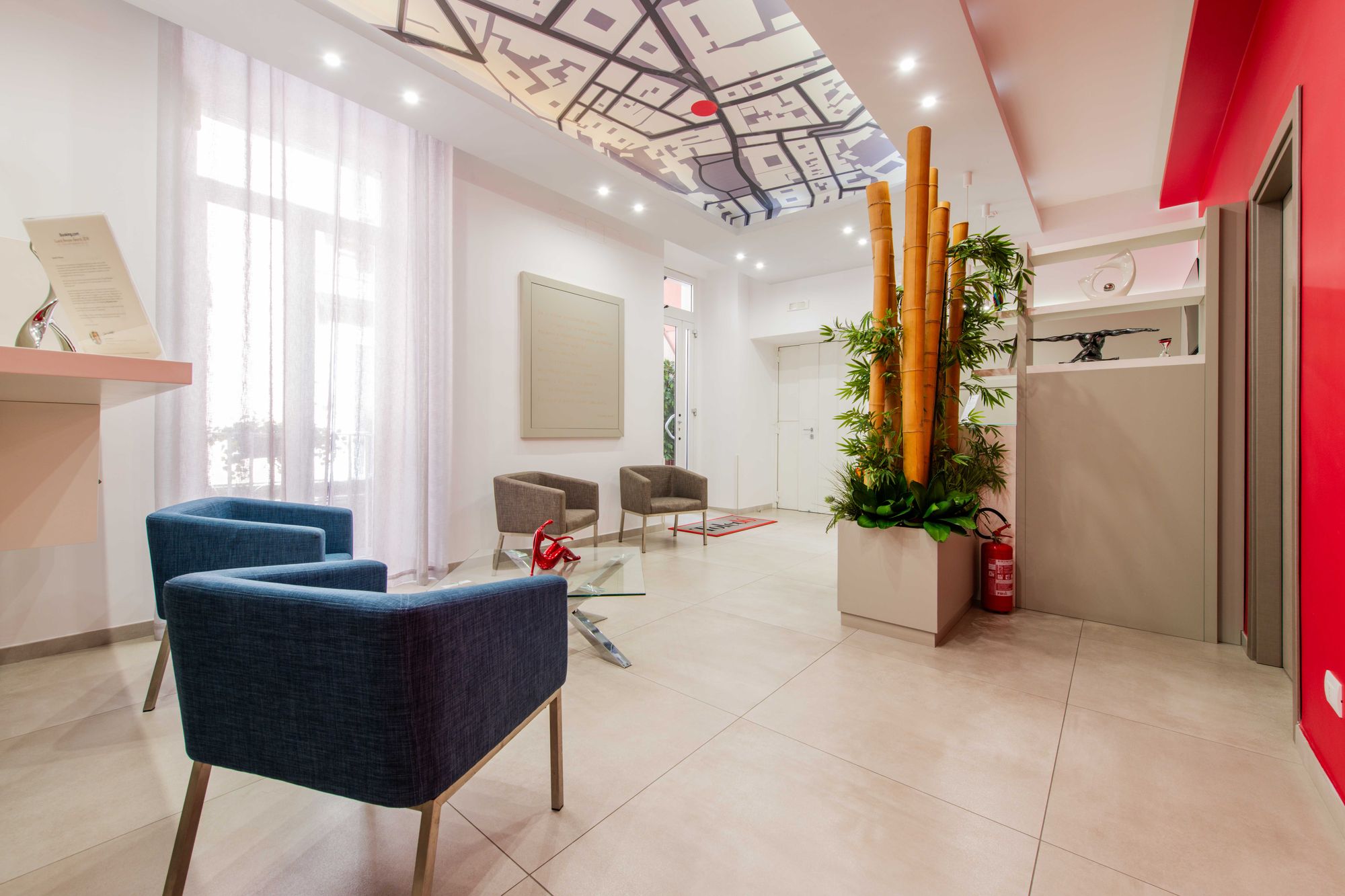 Reception con banco bianco, parete rossa e canne di bambù decorative - Toledo16 Luxury Suites Napoli, Via Toledo 16