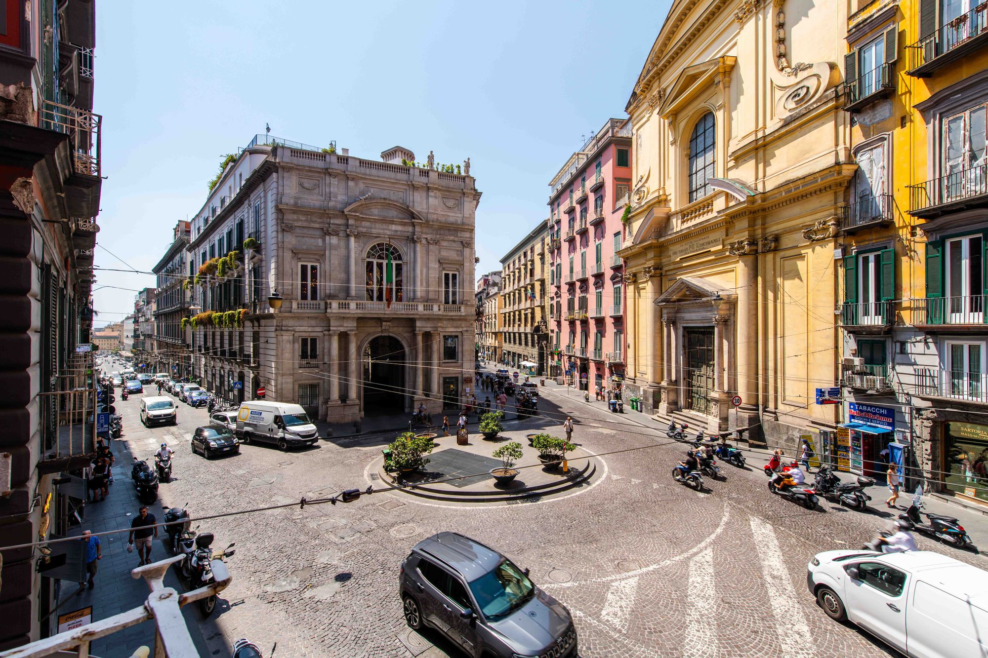 Vista panoramica dal balcone su un incrocio del centro storico di Napoli con palazzo storico, facciata di chiesa e traffico di auto e scooter - Toledo16 Luxury Suites Napoli