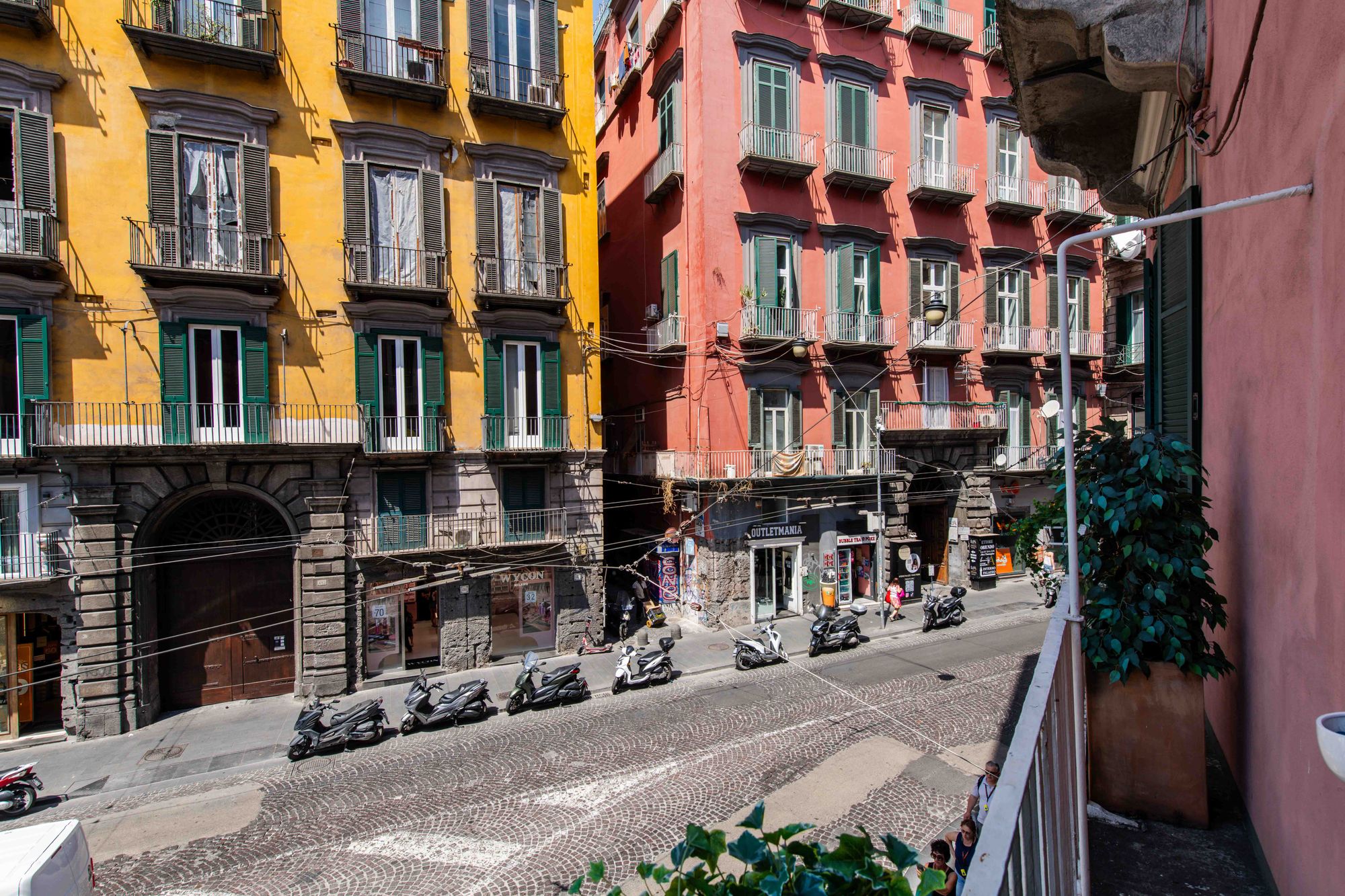 Vista dal balcone sui palazzi colorati giallo e corallo di una strada del centro di Napoli con scooter parcheggiati - Toledo16 Luxury Suites Napoli