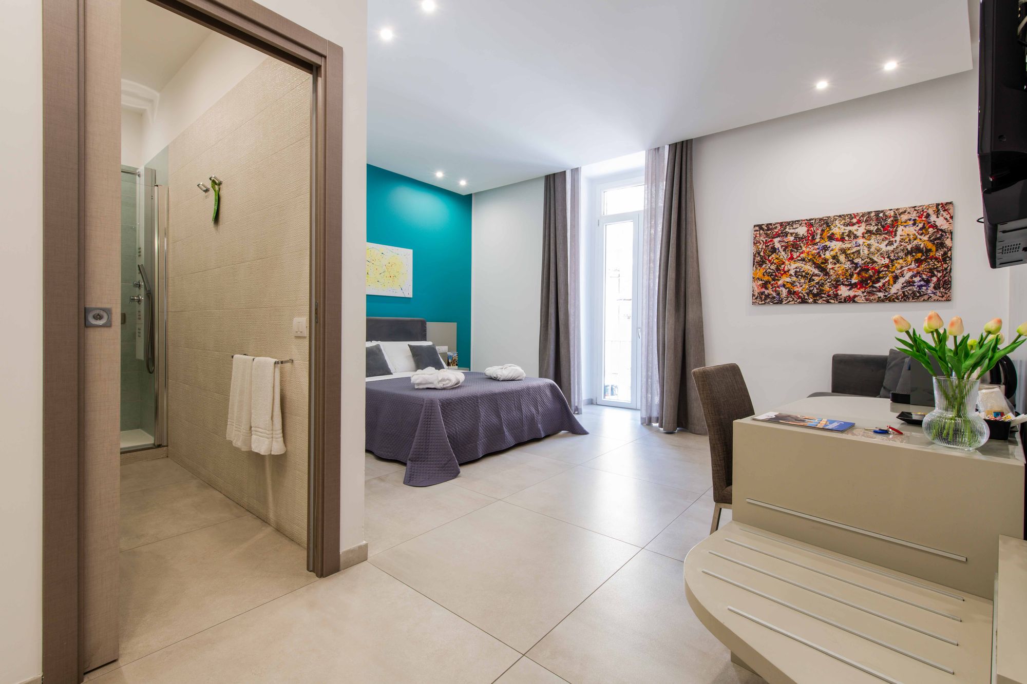 Corridoio d'ingresso con doccia a vista sulla sinistra e vista sulla camera con parete turchese e letto matrimoniale in fondo - Toledo16 Luxury Suites Napoli