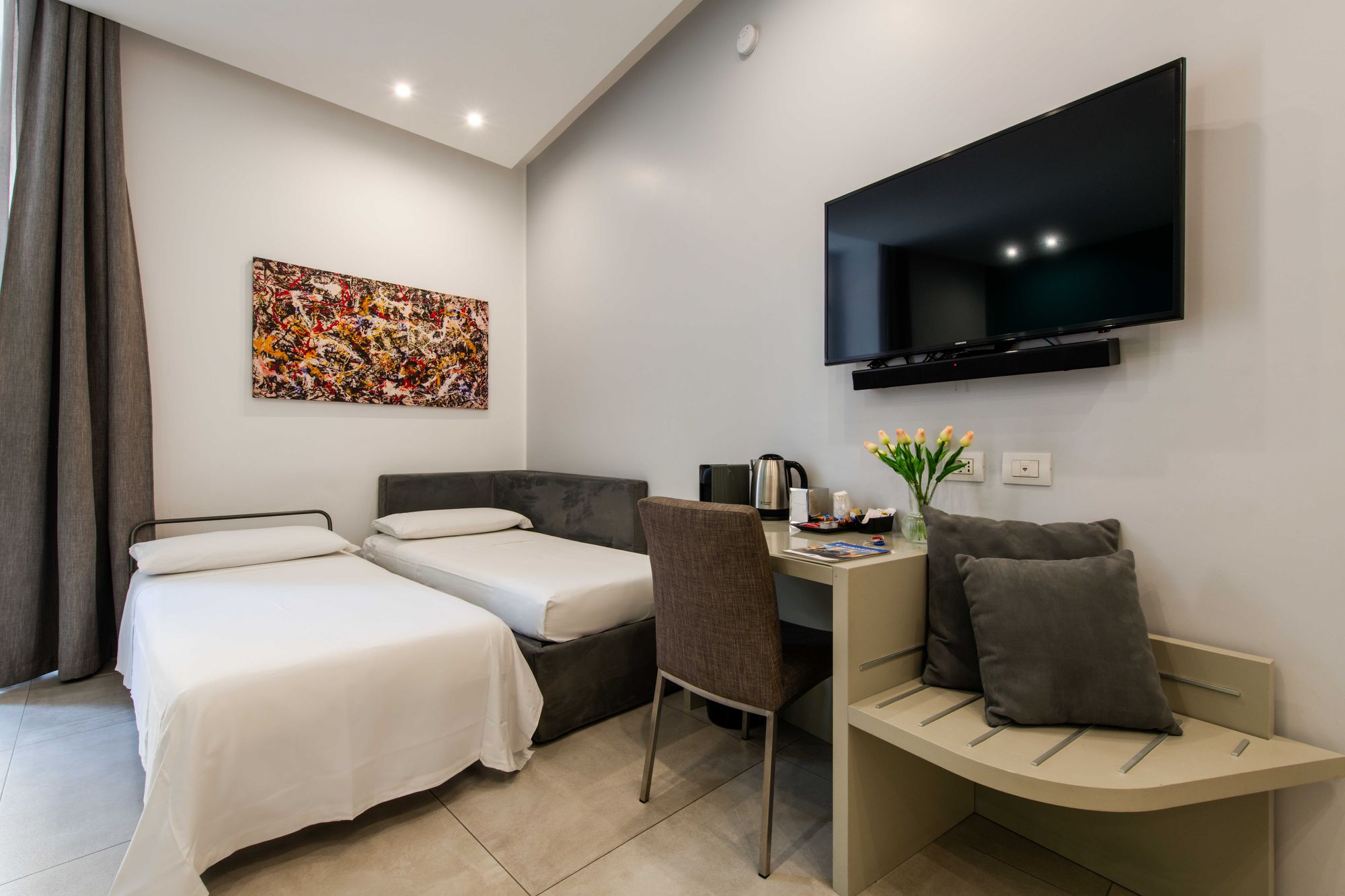 Vista d'insieme della suite con letto aggiuntivo, divano letto grigio, scrivania e tende alla finestra - Toledo16 Luxury Suites Napoli