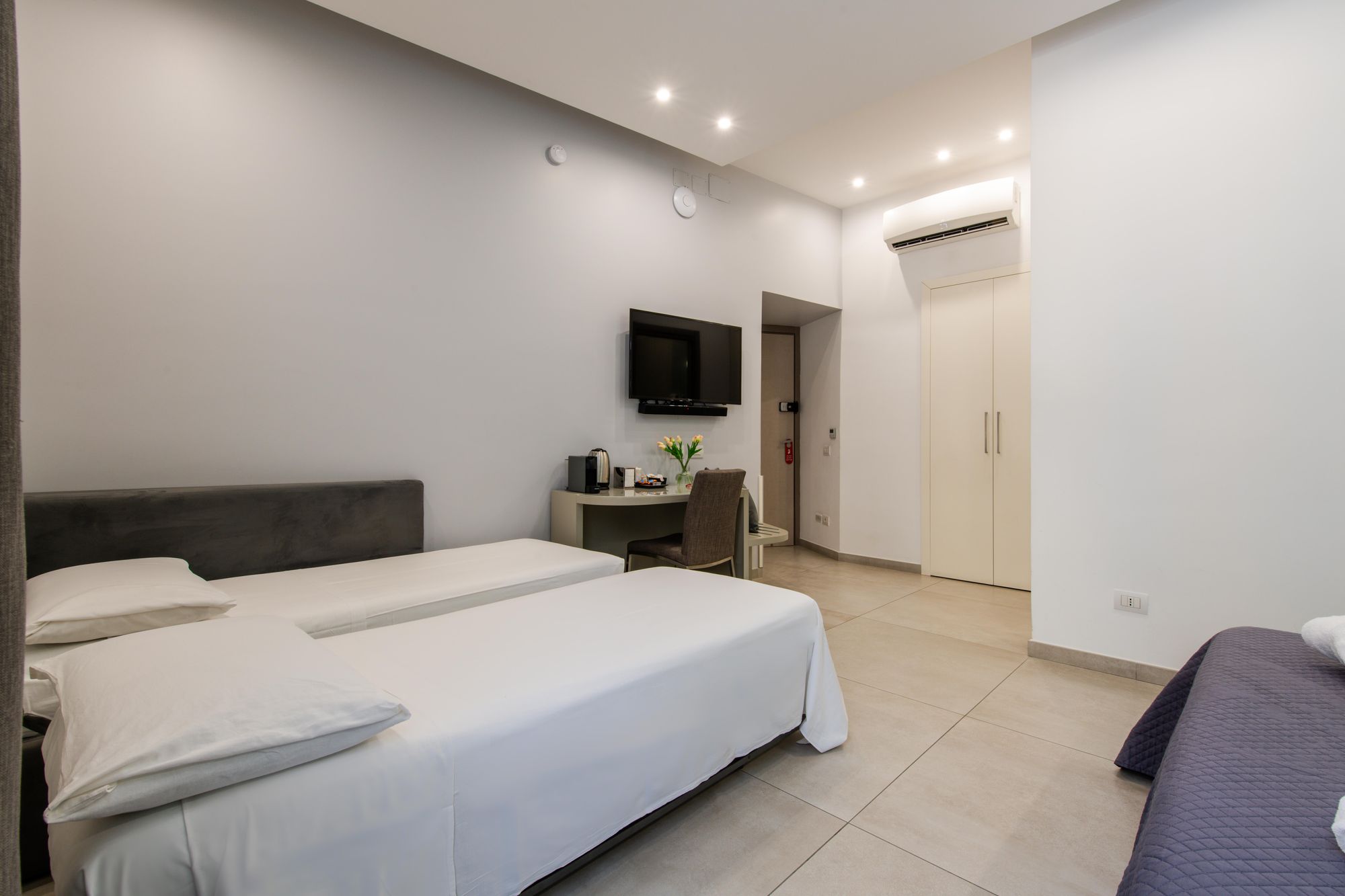 Letto aggiuntivo con lenzuola bianche, armadio guardaroba e climatizzatore a parete sullo sfondo della suite - Toledo16 Luxury Suites Napoli