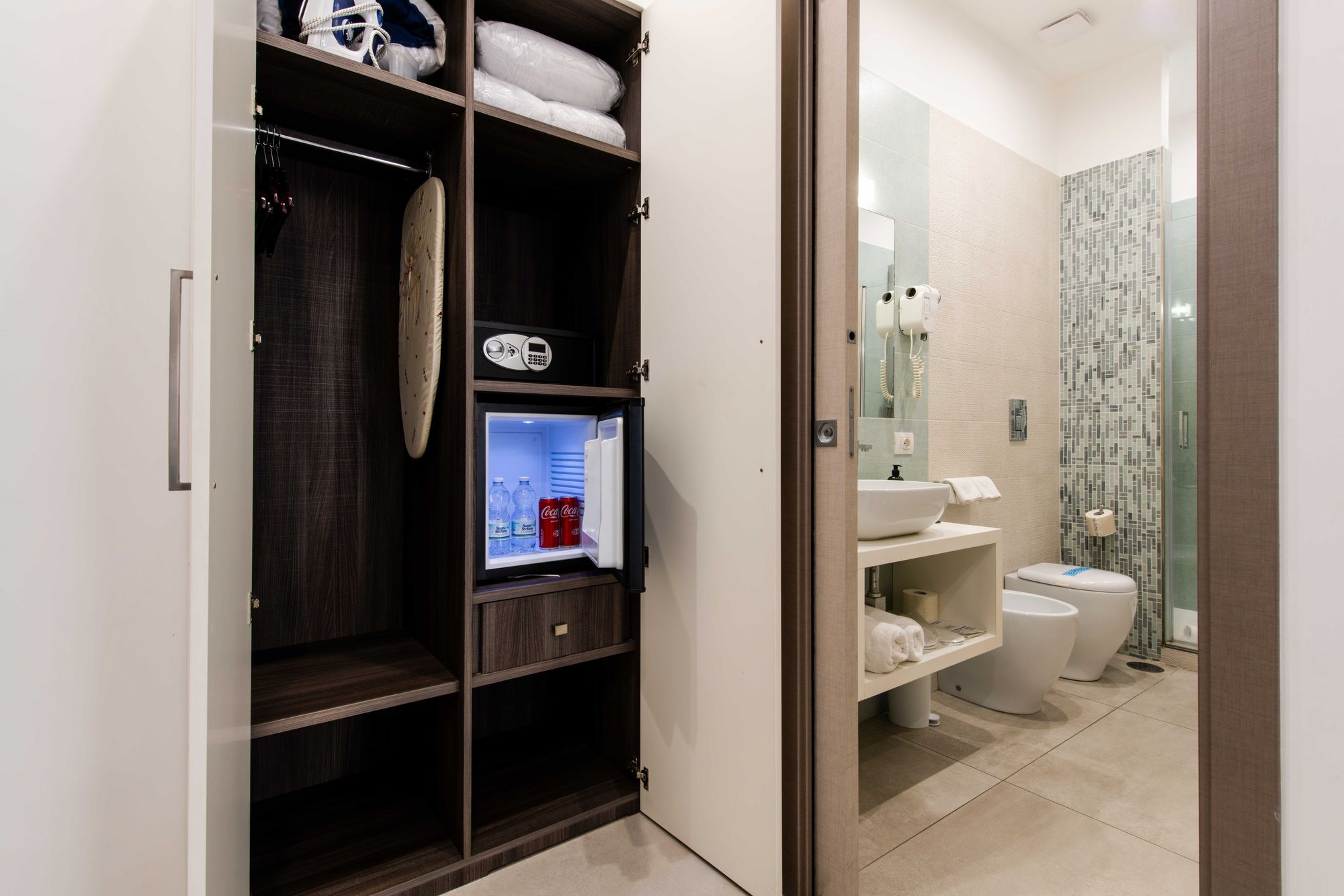 Armadio guardaroba con cassaforte, minibar con bibite, asse da stiro e scorcio del bagno con doccia e sanitari sullo sfondo - Toledo16 Luxury Suites Napoli