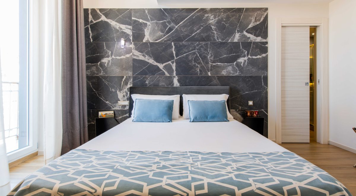 Camera con parete in marmo grigio, letto matrimoniale con cuscini azzurri e copriletto geometrico, Municipio Luxury Suite Napoli