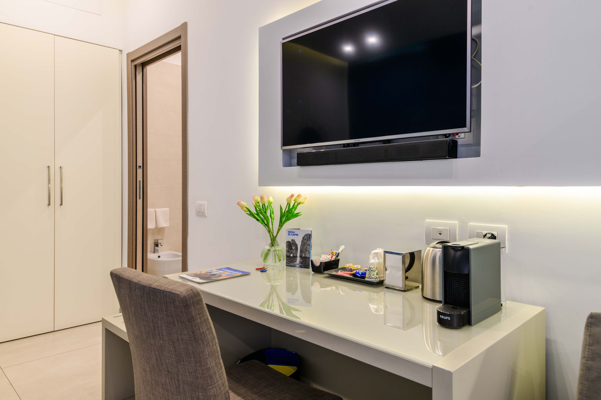 Letto con testiera grigia, cuscini bianchi e grigi, quadro colorato sulla parete blu e comodino con cartolina - Toledo16 Luxury Suites Napoli