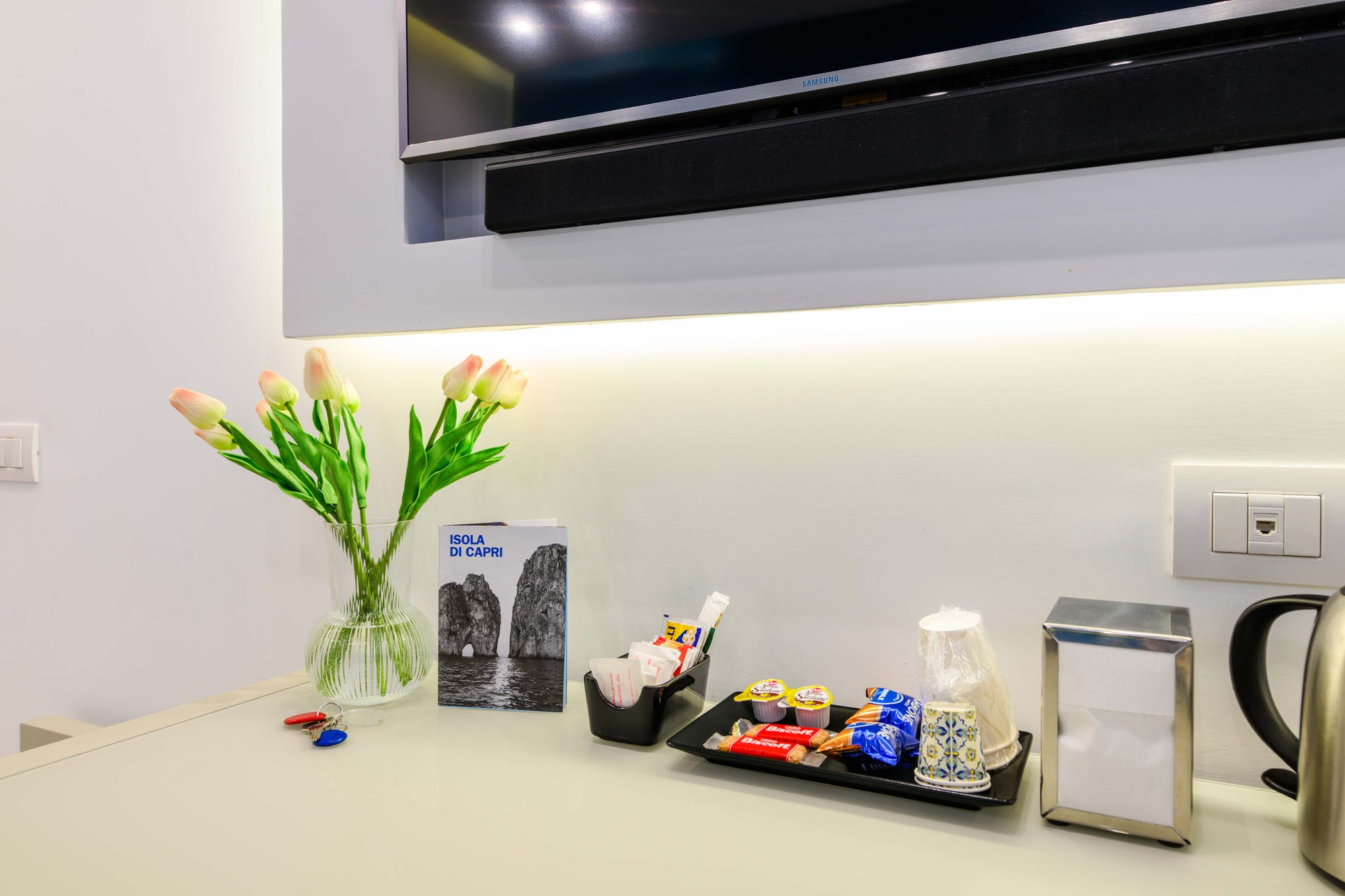 Dettaglio della scrivania con TV e soundbar, tulipani, guida di Capri, vassoio di benvenuto e bollitore - Toledo16 Luxury Suites Napoli