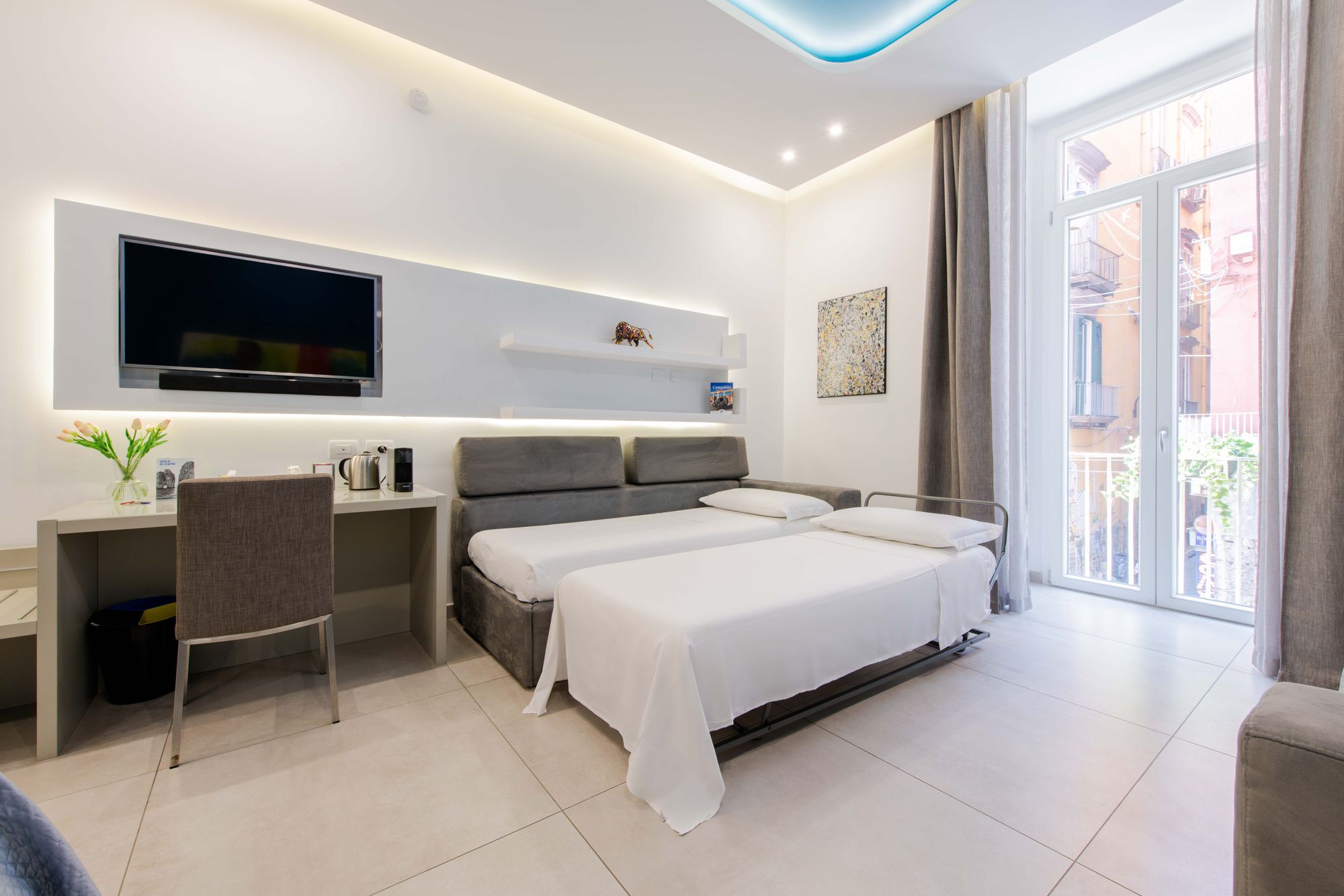 Suite con divano letto apribile a due singoli, TV a parete, mensola con statuetta di toro, scrivania e balcone - Toledo16 Luxury Suites Napoli