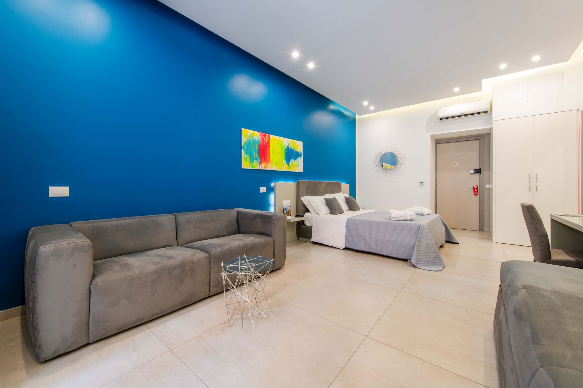 Divano grigio con tavolino in vetro e metallo, mensola con statuetta di toro, scrivania e armadio bianco sullo sfondo - Toledo16 Luxury Suites Napoli