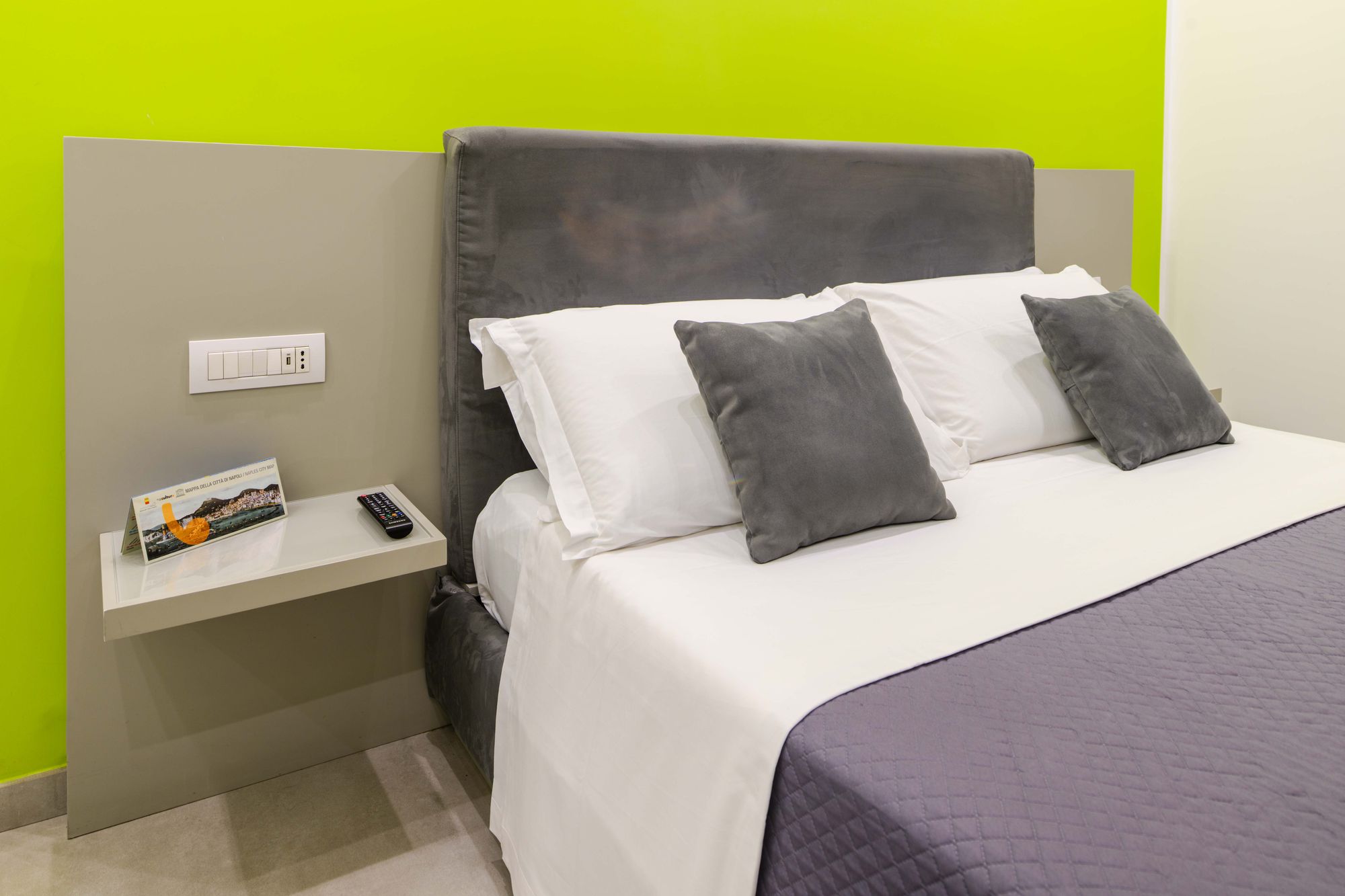 Testiera in velluto grigio del letto matrimoniale con cuscini bianchi e grigi, comodino sospeso su parete verde lime, camera Napoli centro - Toledo16 Luxury Suites Napoli