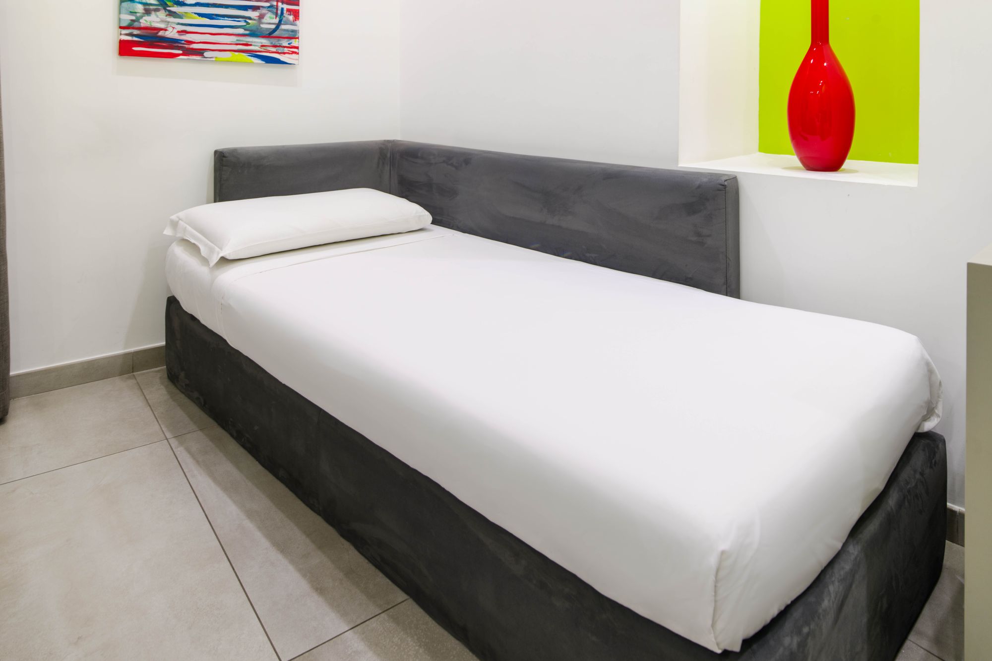 Terzo letto singolo ad angolo con testiera grigia in velluto, quadro colorato e nicchia con vaso rosso, camera tripla Napoli - Toledo16 Luxury Suites Napoli