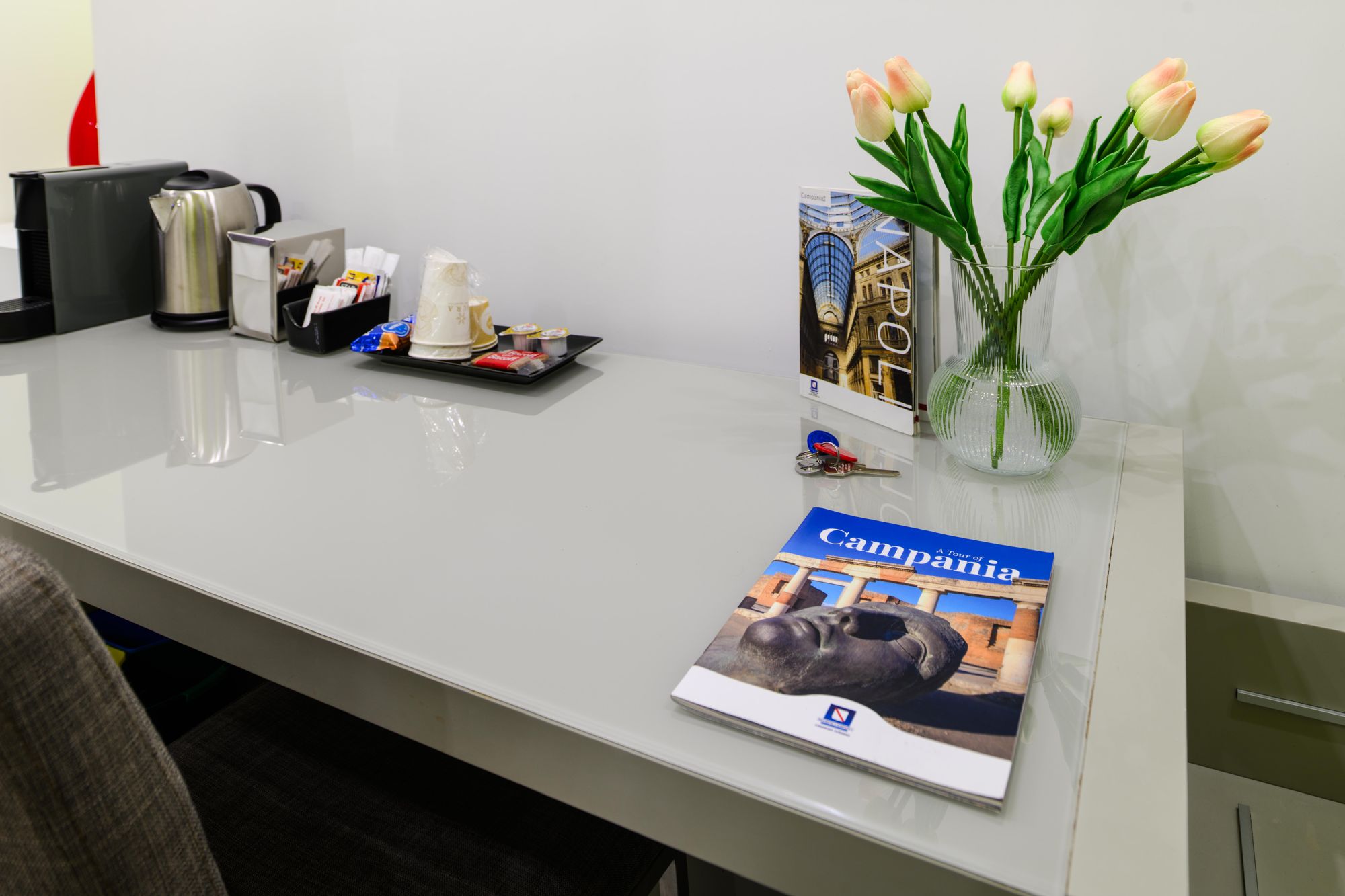 Scrivania con guida turistica di Napoli, rivista sulla Campania, mazzo di chiavi e vaso di tulipani, camera Napoli centro - Toledo16 Luxury Suites Napoli