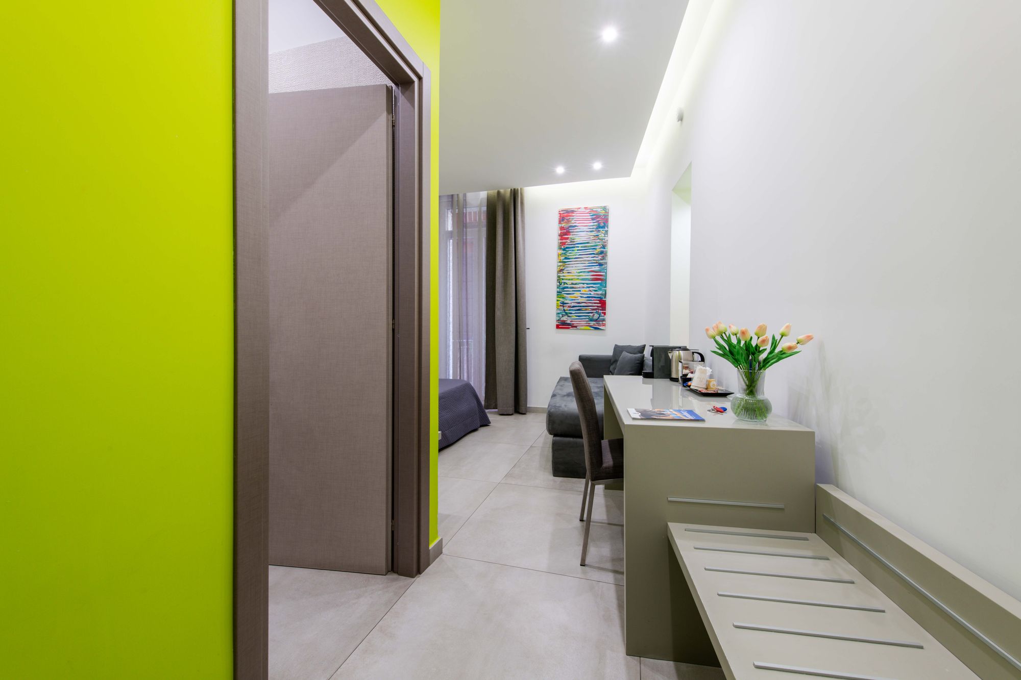 Corridoio d'ingresso con parete verde lime e porta del bagno aperta, vista su scrivania con vaso di tulipani e divano, camera Napoli centro - Toledo16 Luxury Suites Napoli
