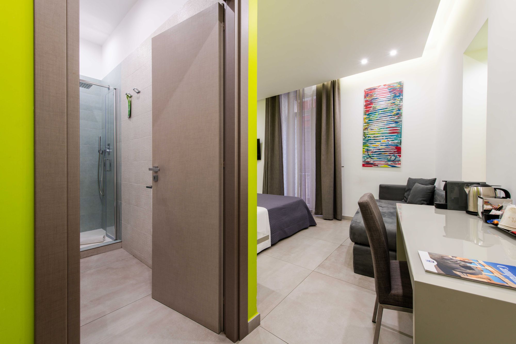Corridoio con porta del bagno aperta e box doccia in vetro visibile, vista sulla camera con letto dal copriletto viola e divano grigio, B&B Napoli centro - Toledo16 Luxury Suites Napoli