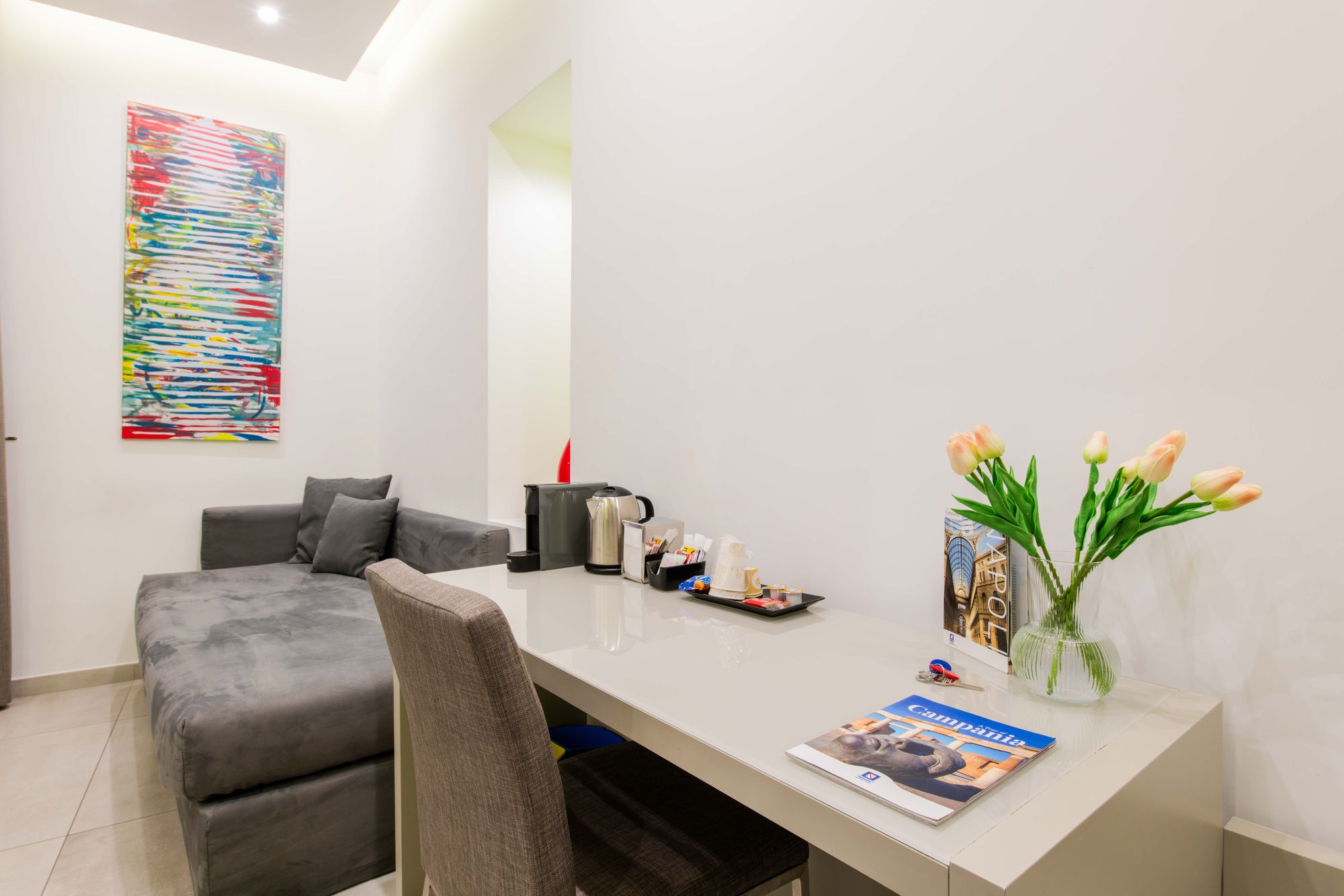Scrivania con macchina da caffè, bollitore, vassoio di snack e vaso di tulipani, angolo relax della camera B&B Napoli - Toledo16 Luxury Suites Napoli