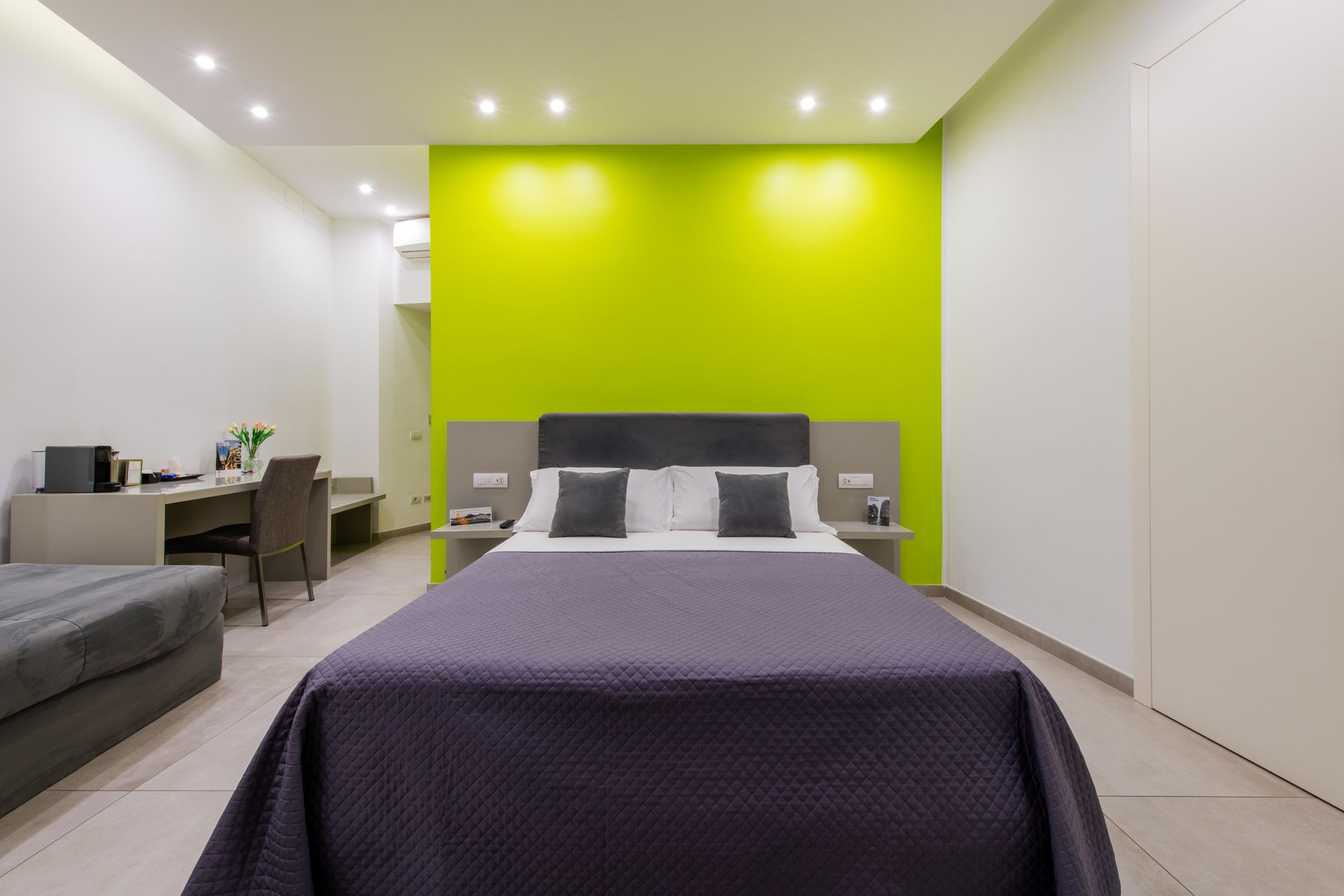 Vista d'insieme della camera con parete verde lime, letto matrimoniale, TV a parete e angolo scrivania con divano, B&B Napoli centro - Toledo16 Luxury Suites Napoli