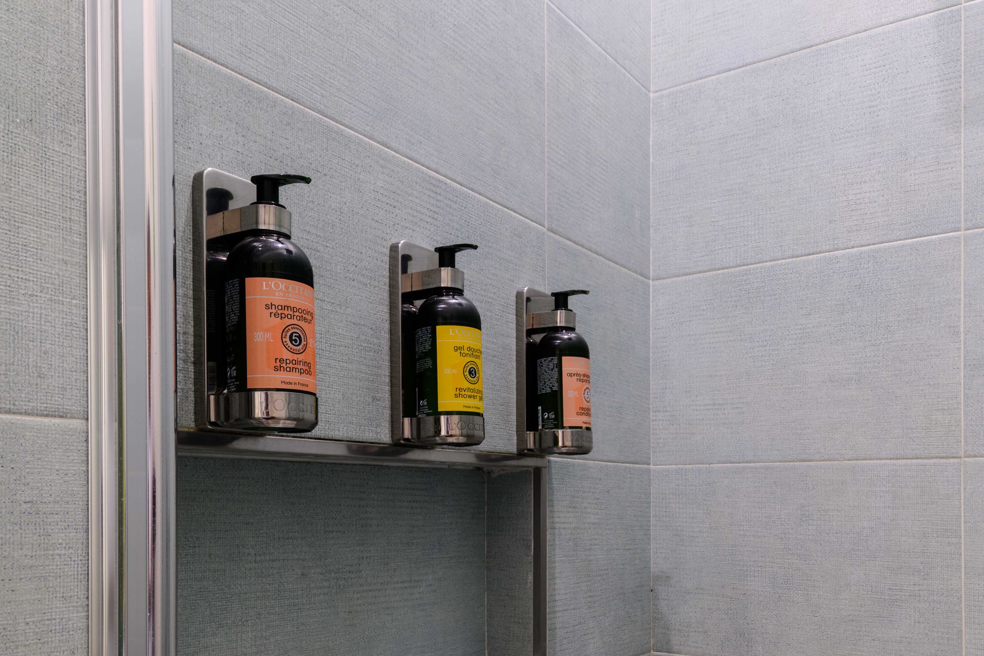 Mensola della doccia con flaconi L'Occitane di shampoo riparatore, gel doccia e balsamo - Toledo16 Luxury Suites Napoli