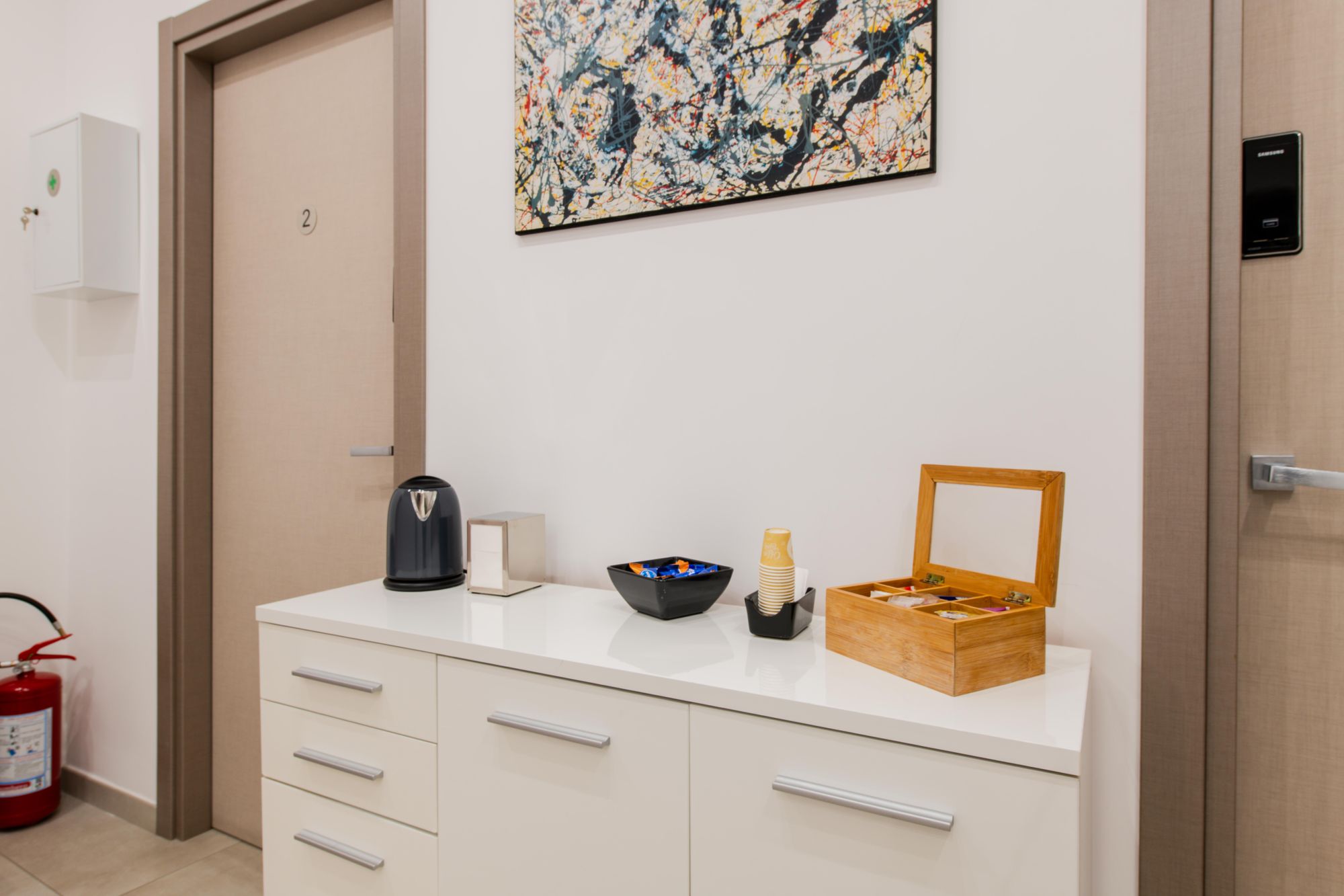 Mobile bianco con bollitore, kit di benvenuto e quadro astratto accanto alla porta della camera 2, Toledo16 Luxury Suites Napoli