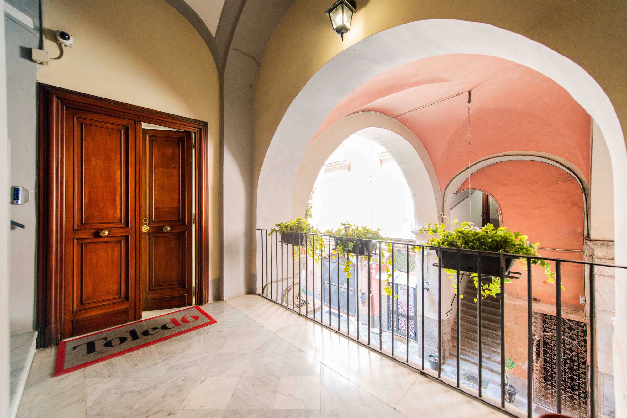 Ballatoio con volte affrescate, ringhiera in ferro battuto e piante, porta d'ingresso in legno con tappeto Toledo16, Napoli centro