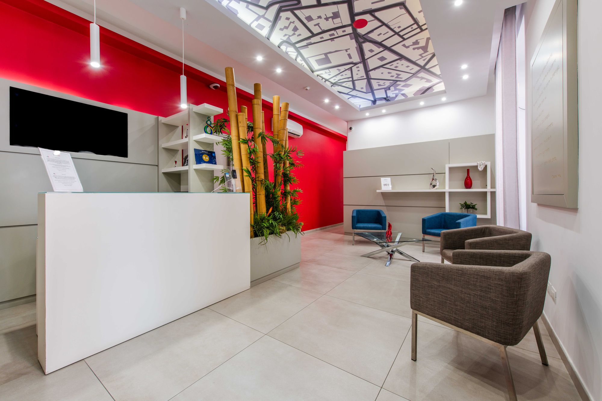 Reception con banco bianco e parete rossa, canne di bambù decorative e poltrone blu, Toledo16 Luxury Suites Napoli
