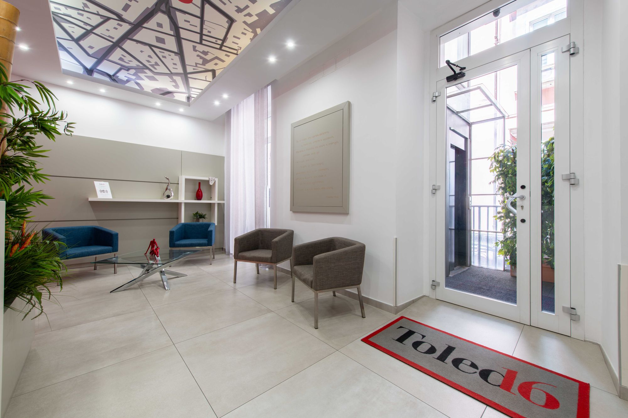 Area salotto con poltrone blu e grigie, tavolino in vetro e porta d'ingresso con tappeto Toledo16, B&B Napoli centro