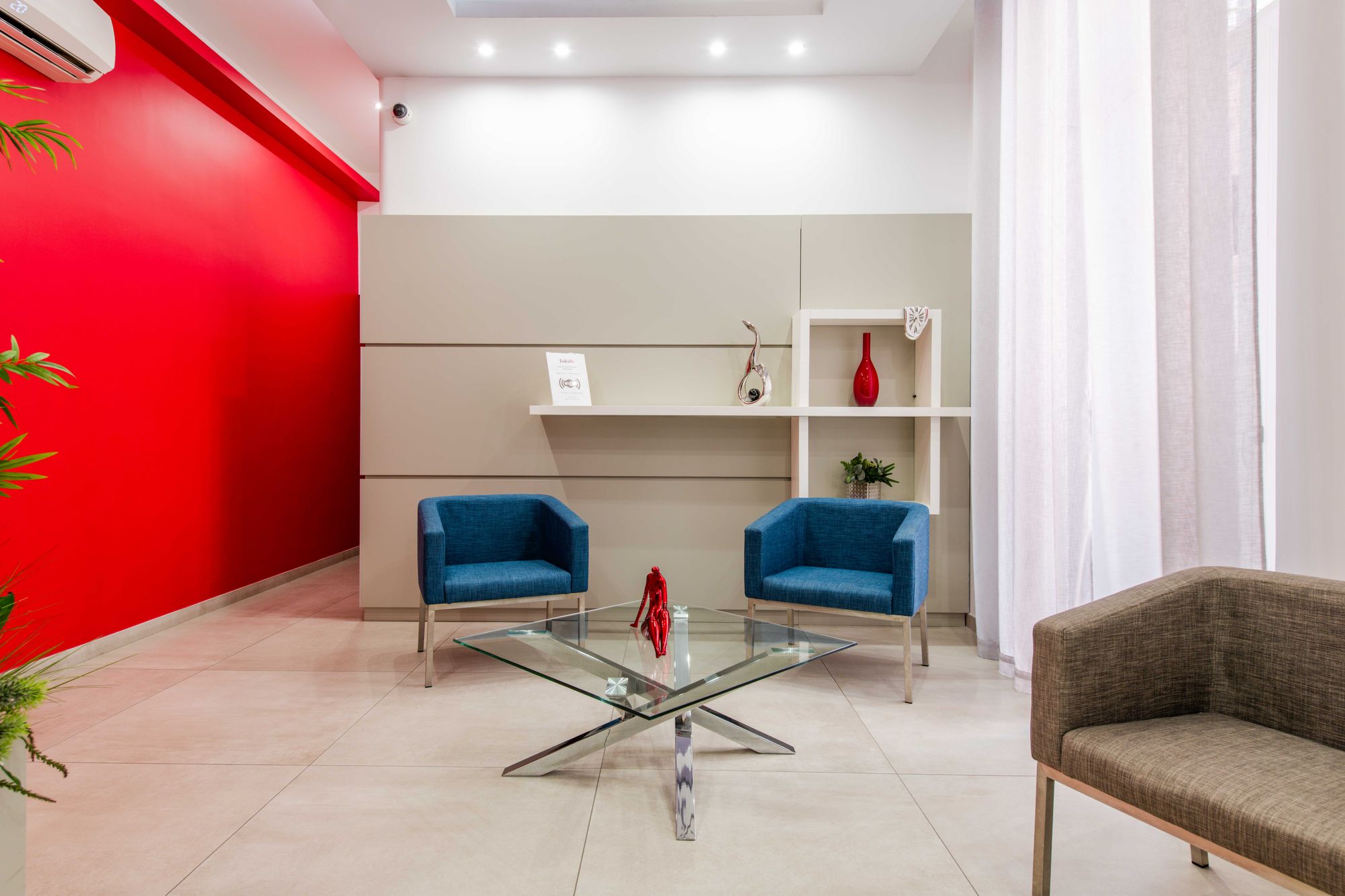 Salotto con parete rossa, poltrone blu e libreria bianca con vaso rosso, Toledo16 Luxury Suites Napoli