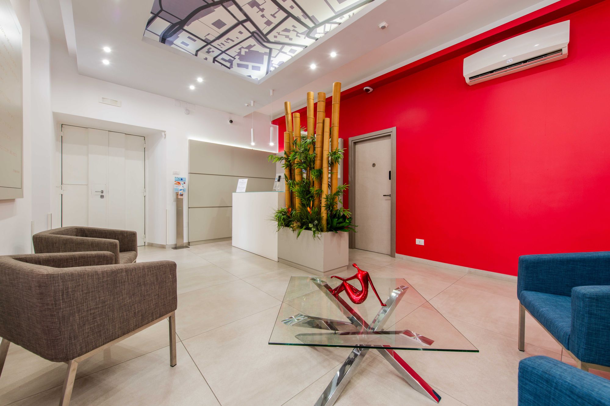 Area lounge con poltrone grigie e blu, reception con bambù decorativo e porta della camera 1, Toledo16 Luxury Suites Napoli