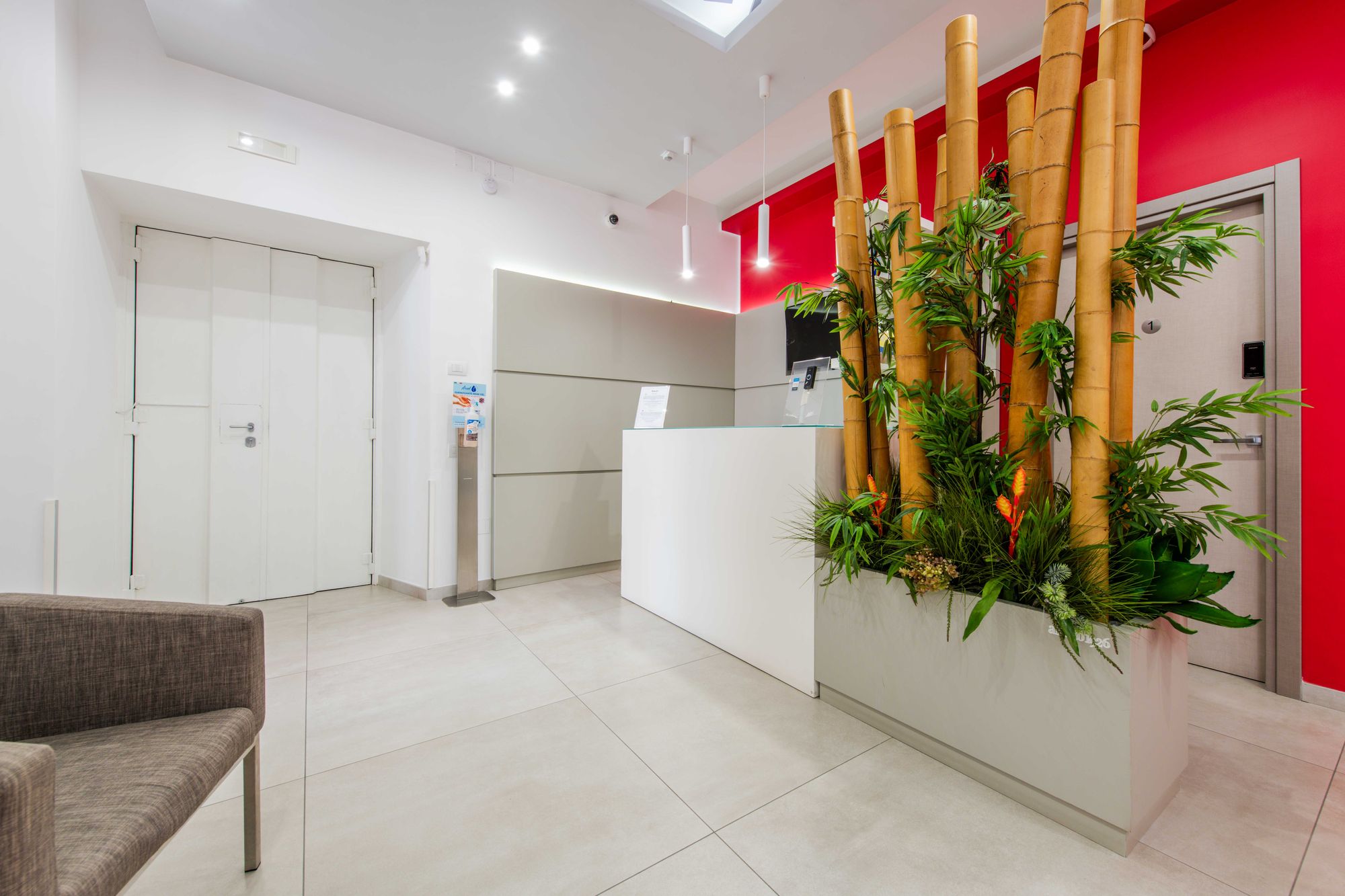 Banco reception bianco con canne di bambù, parete rossa e porta della camera 1, Toledo16 Luxury Suites Napoli