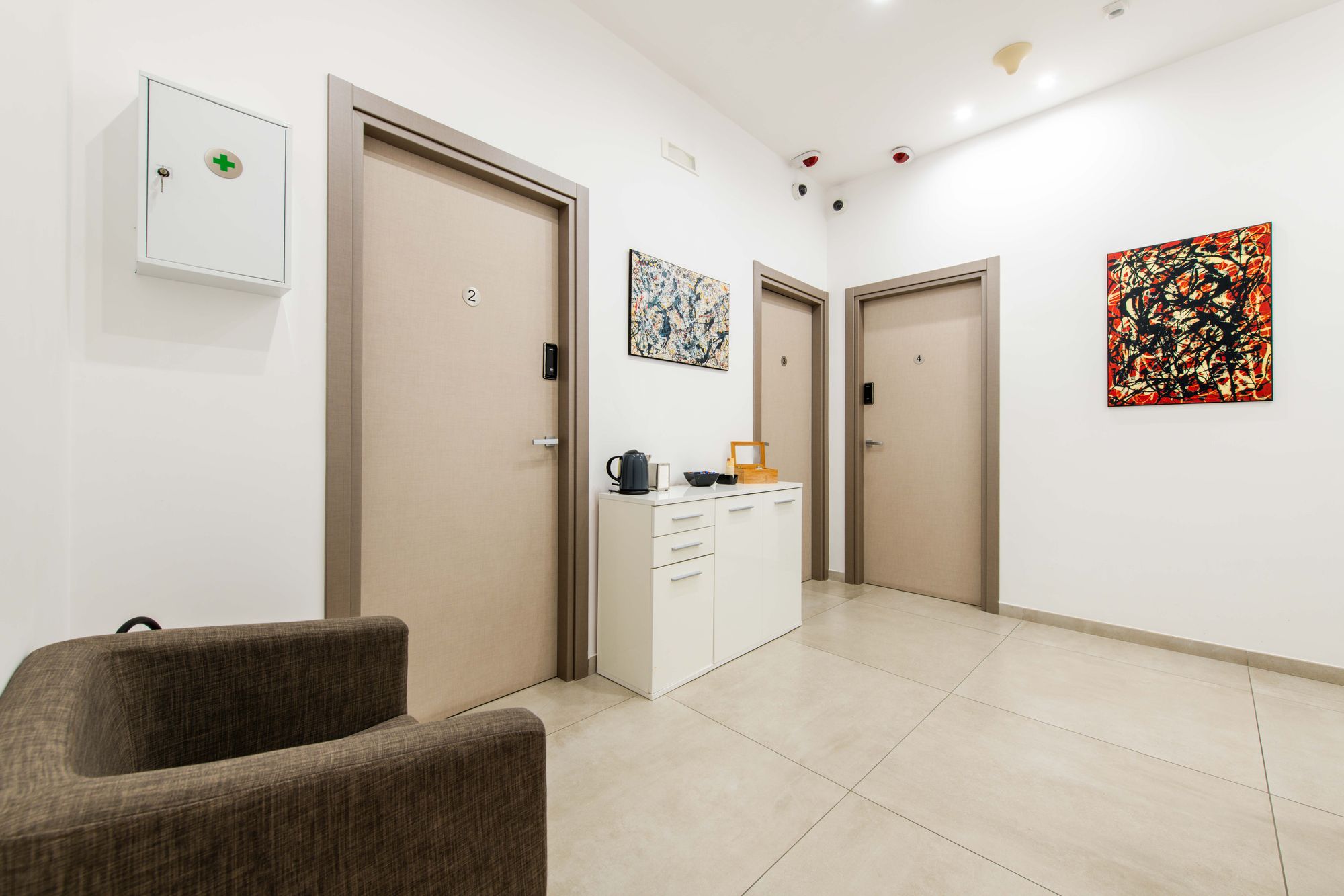Corridoio con porte delle camere 2, 3 e 4, quadri astratti e pavimento in gres chiaro, Toledo16 Luxury Suites Napoli